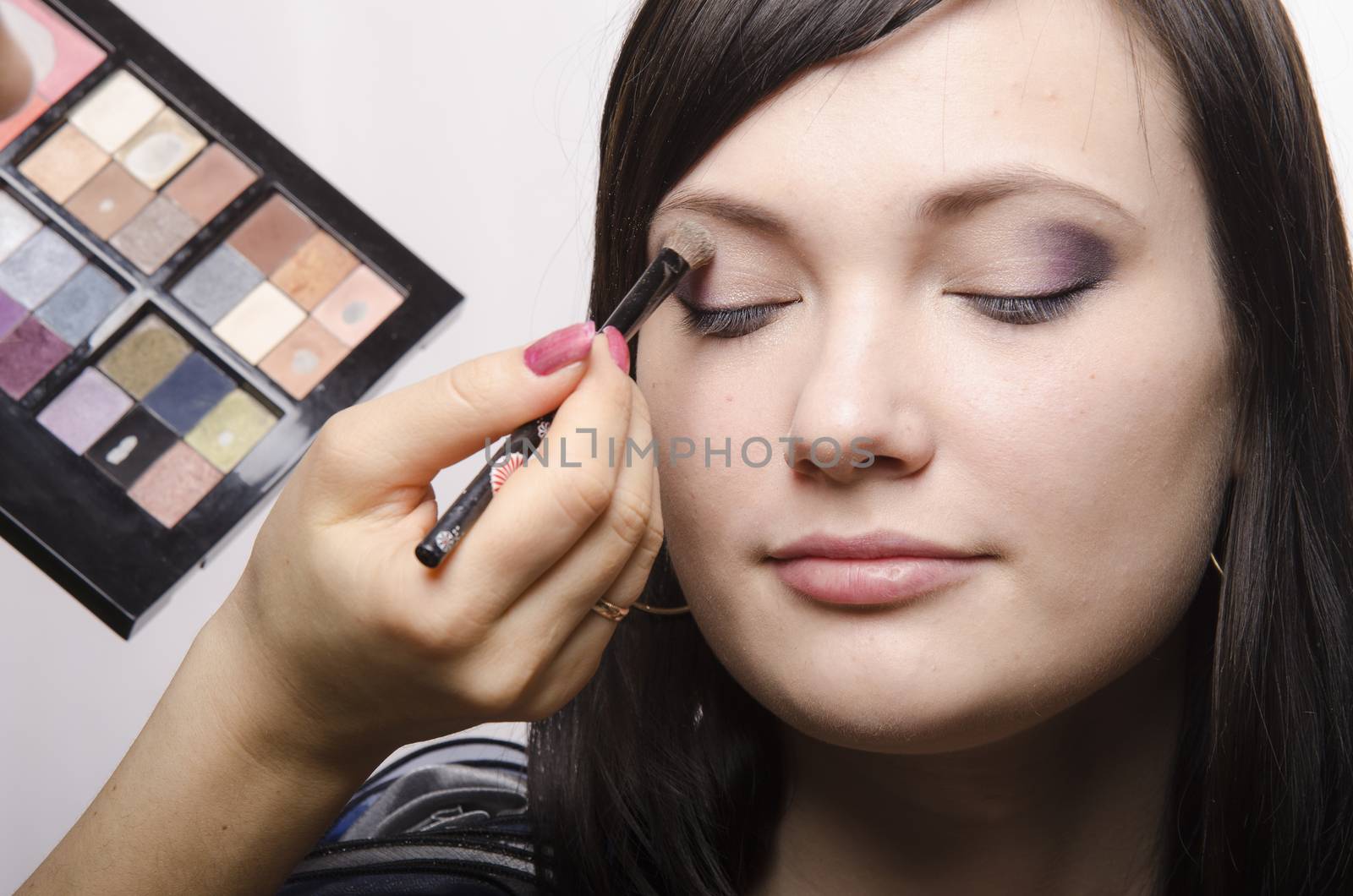 Makeup artist deals makeup on the model's face. She paints the shadows of the upper eyelids model.