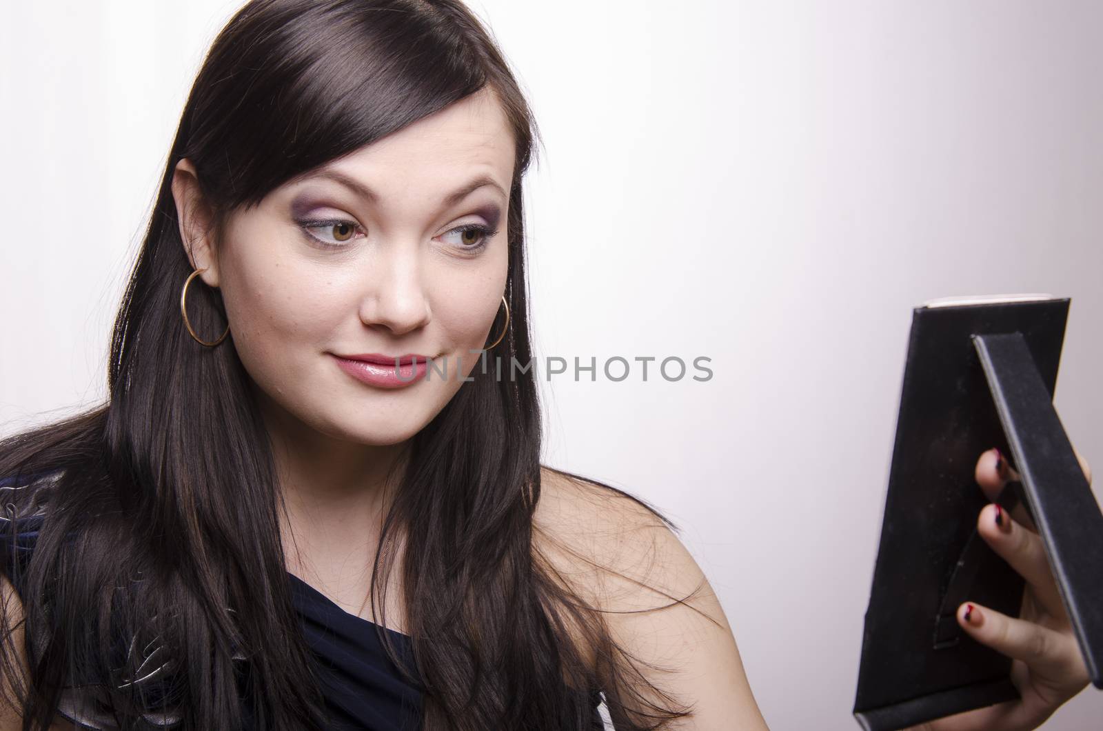 A beautiful young girl looks in the mirror. The girl is very happy with the make-up.