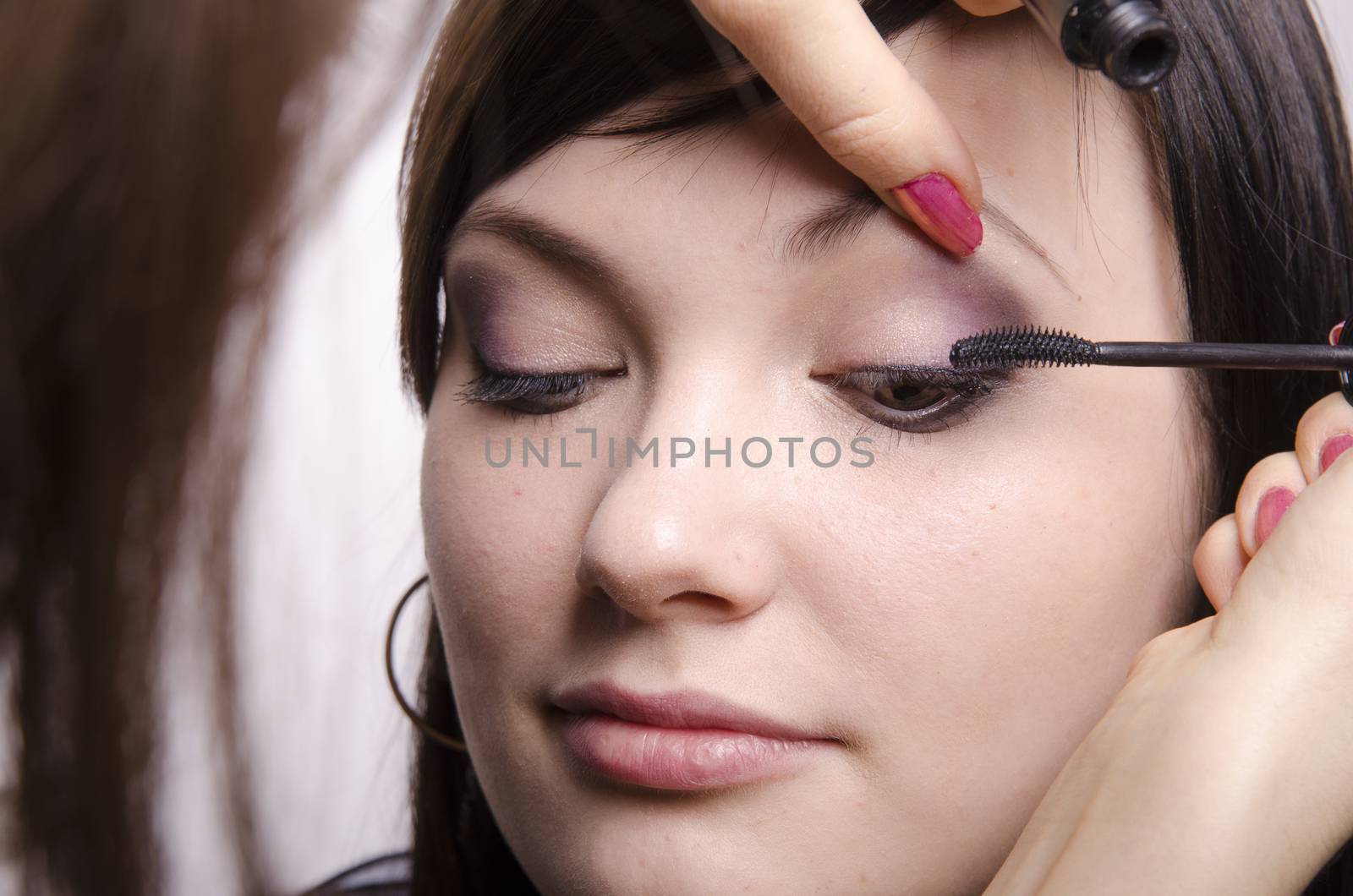 Makeup artist deals makeup on the model's face. She paints eyelashes model.