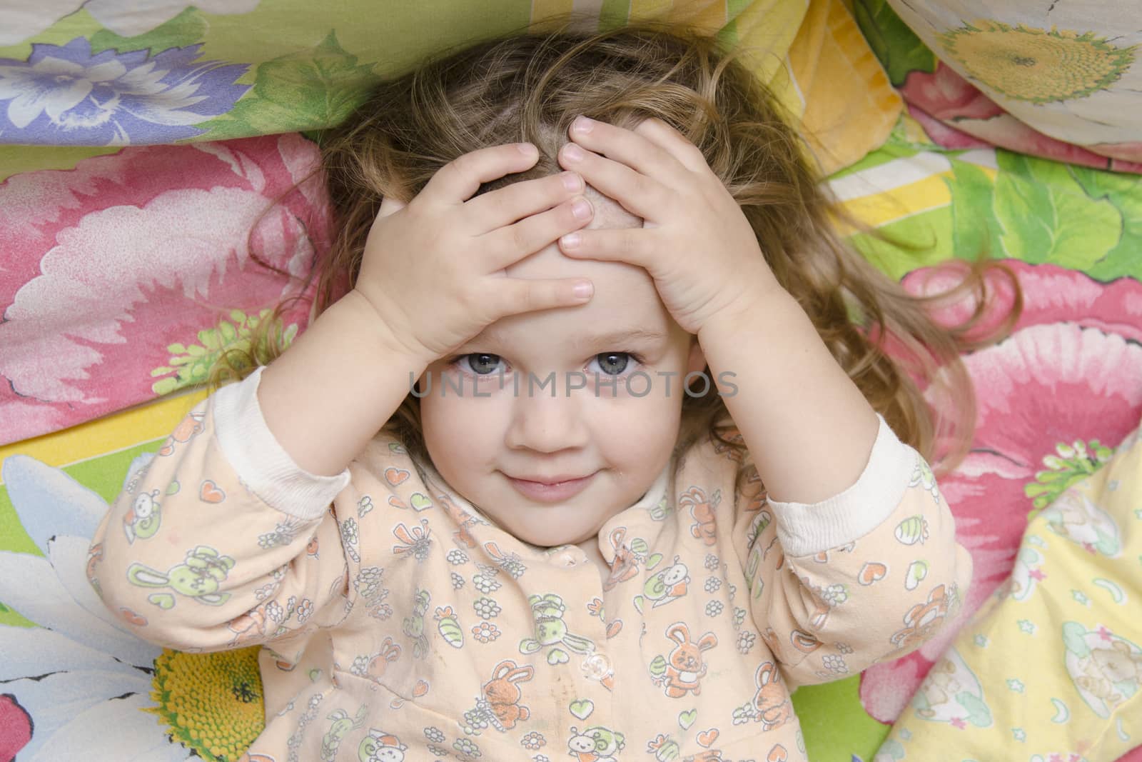 Two-year-old girl is in bed. The girl hugged his head in his hands and fun looking at the picture. Photo above. Portrait