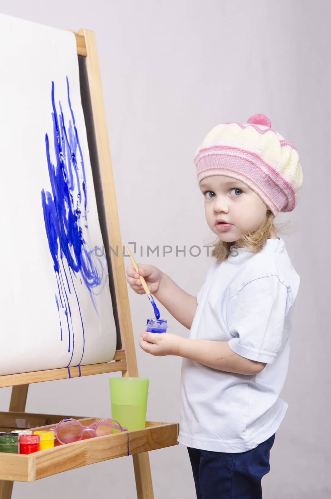 Three-year-old girl playing in the artist. Girl draws on the easel paints