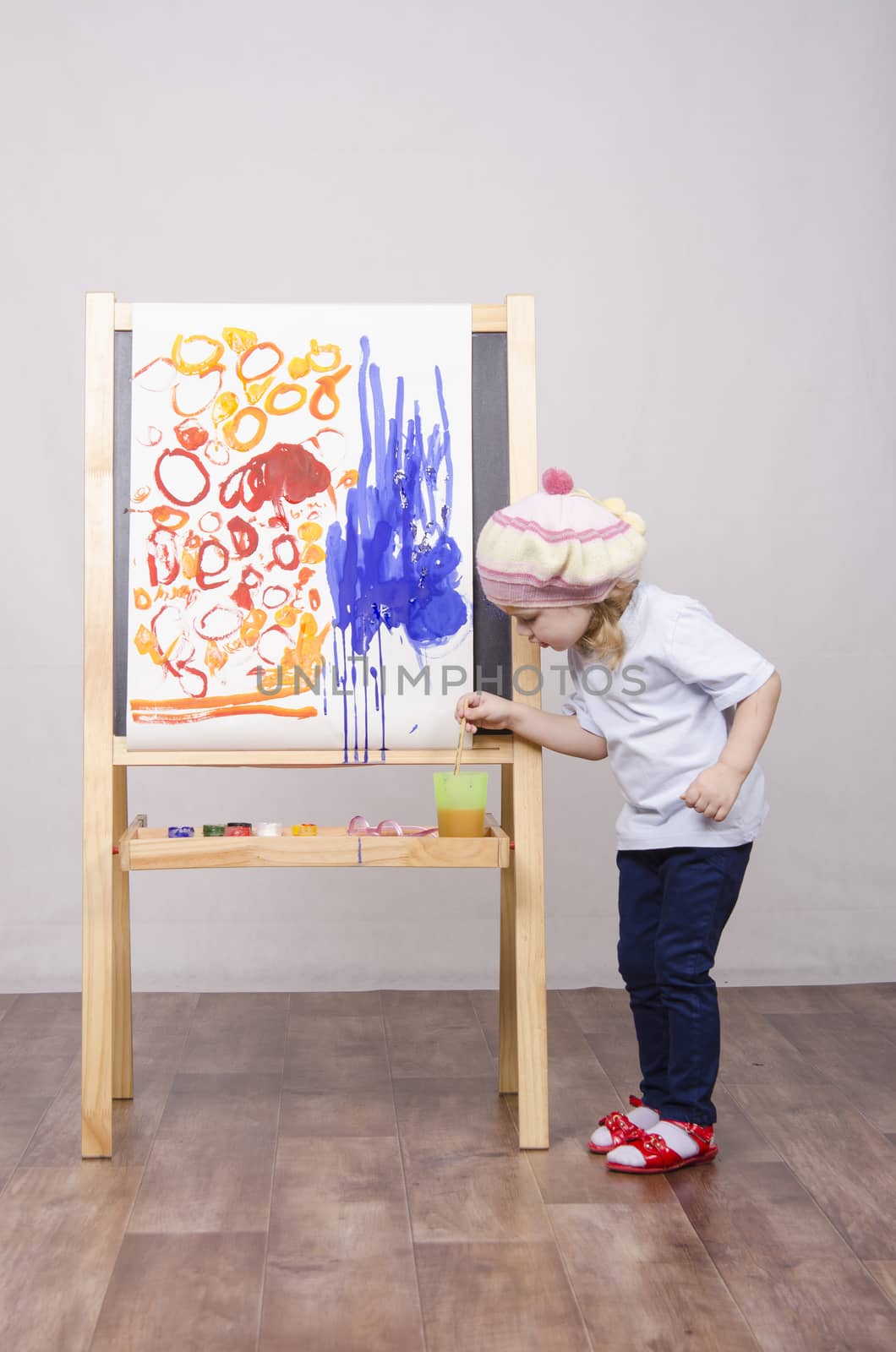 Three-year-old girl playing in the artist. Girl draws on the easel paints