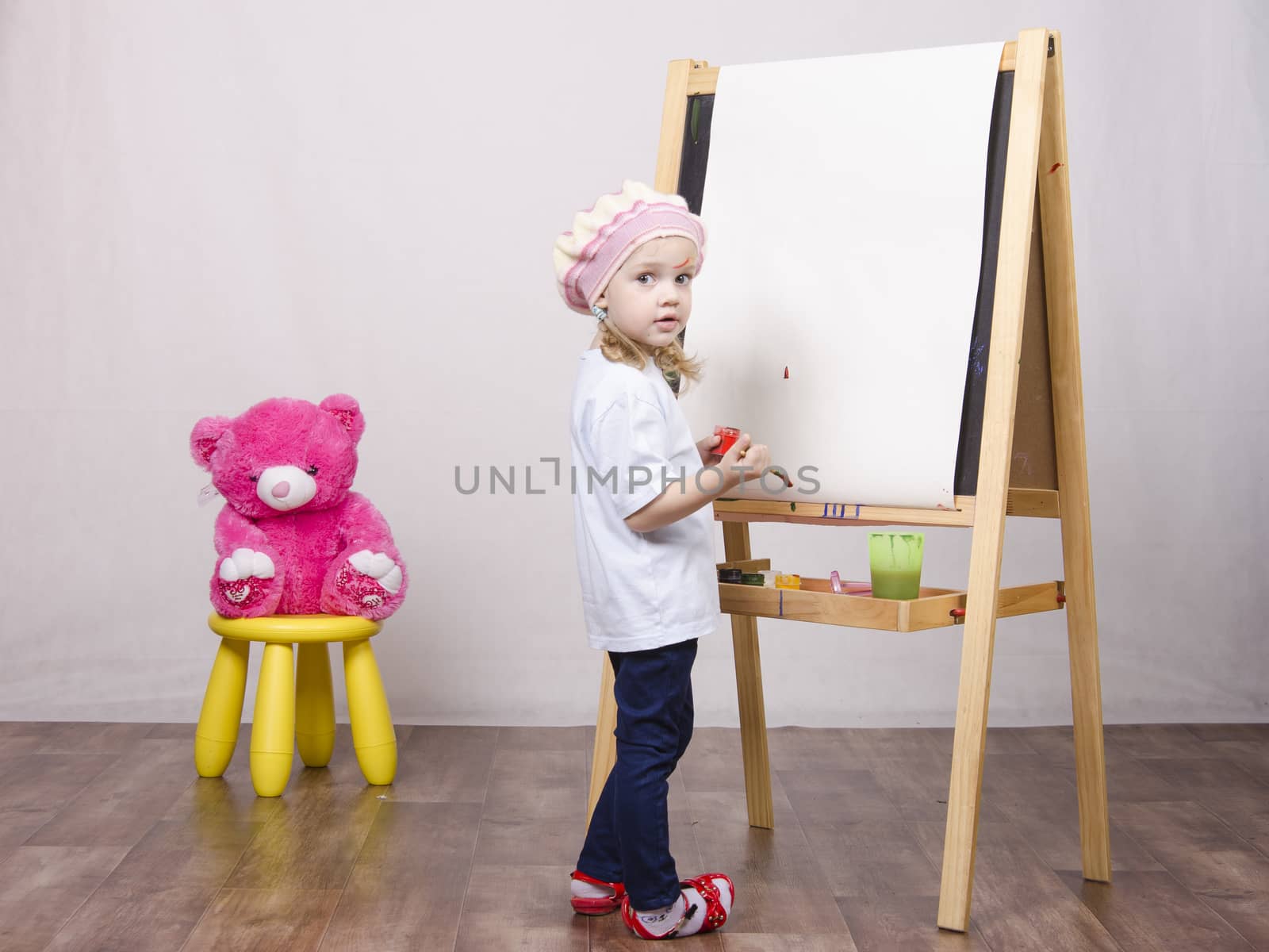 Three-year-old girl playing in the artist. Girl draws on the easel paints bear sitting on a chair