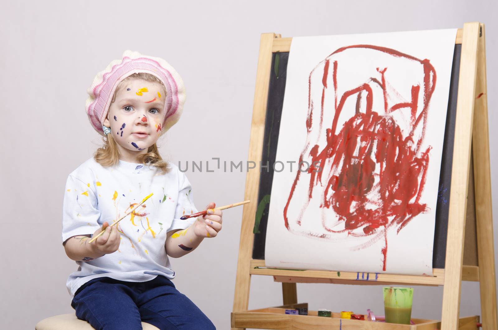 Portrait of a three-year old girl playing in the artist. Girl mud paints. Standing behind you easel