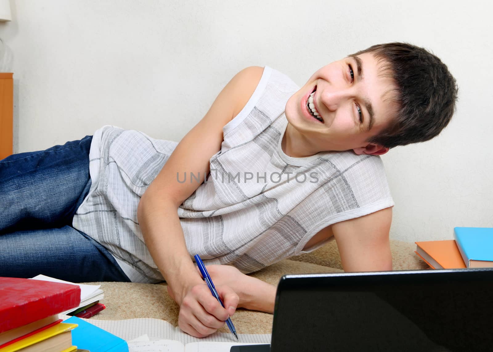 Cheerful Teenager doing Homework on the Sofa at the Home