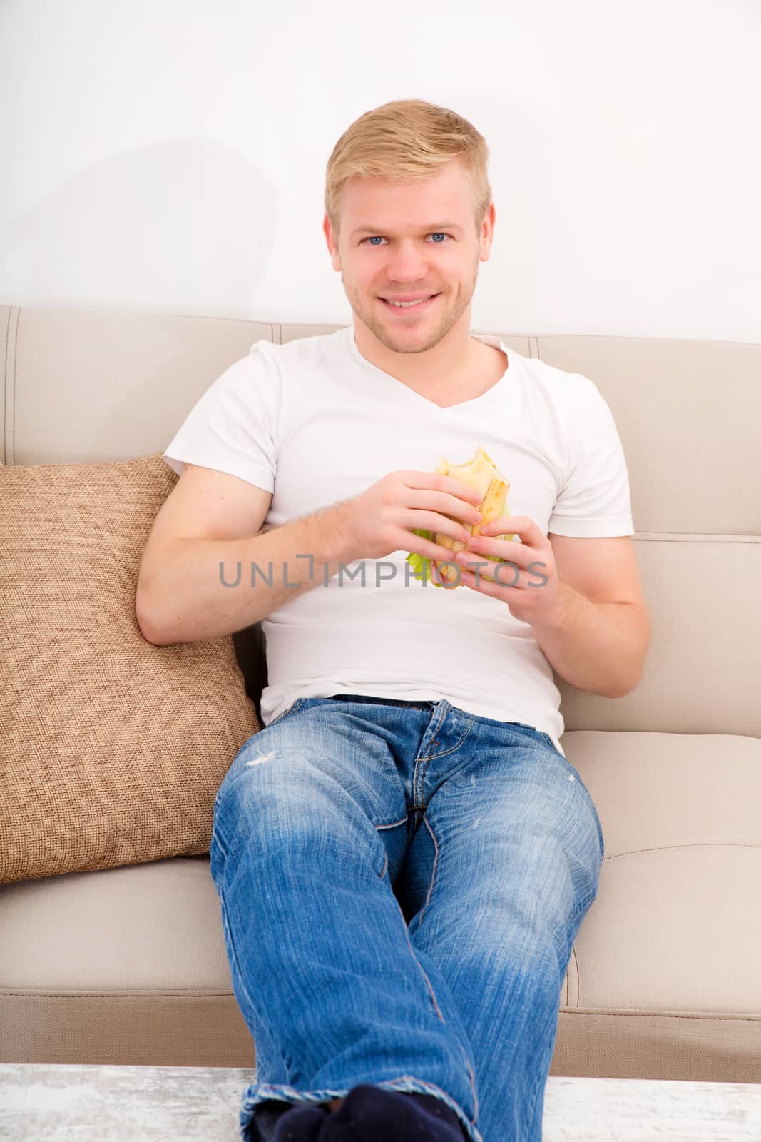 Young man eating a sandwich at home by Spectral
