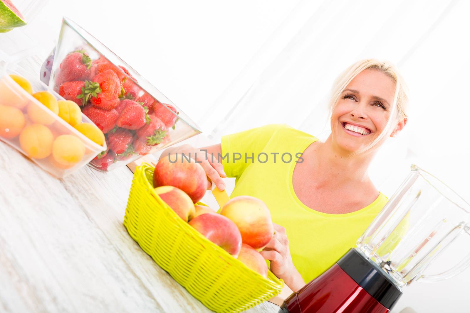 A beautiful mature woman making a smoothie or juice with fruits in the kitchen.