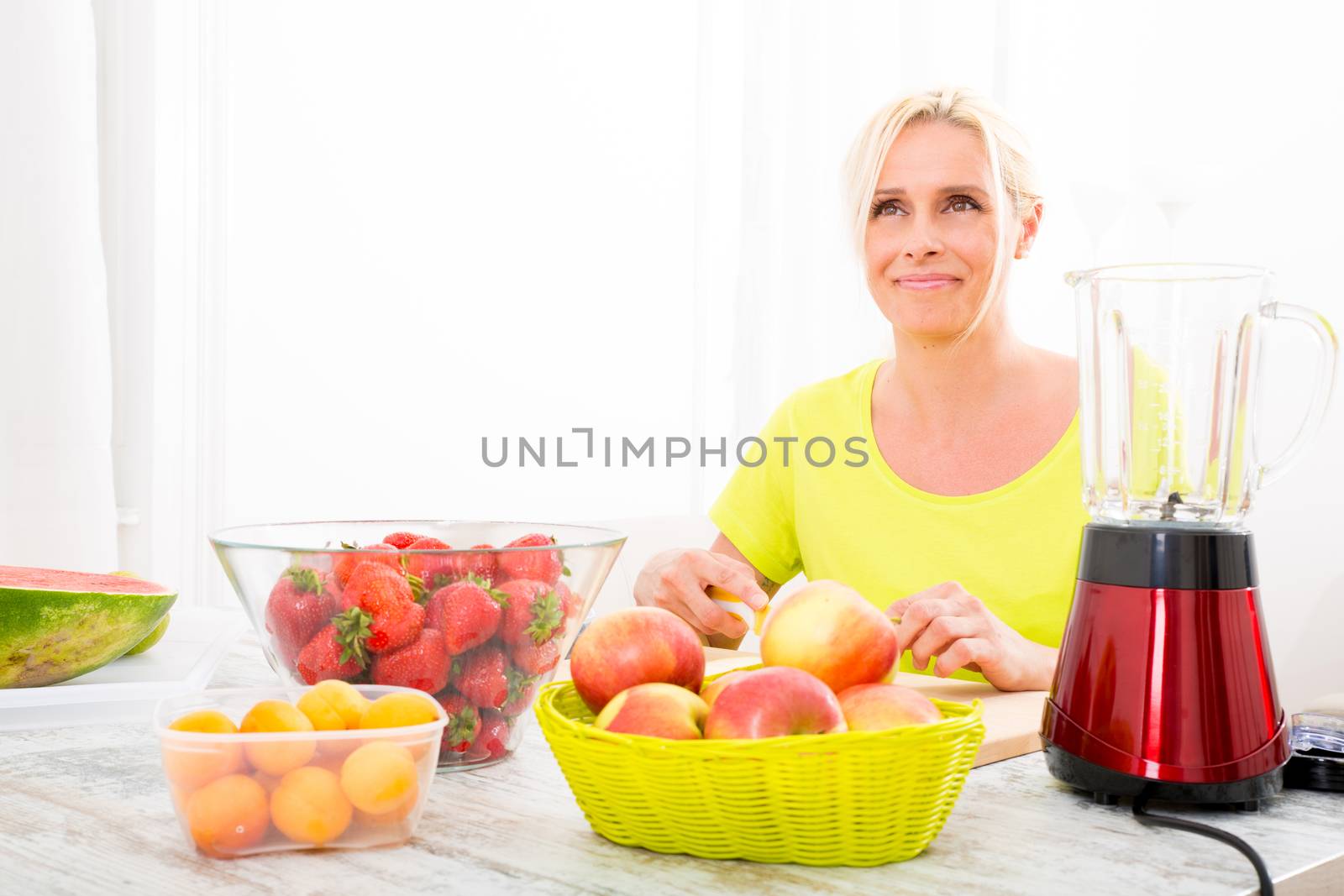 A beautiful mature woman preparing a smoothie or juice with fruits in the kitchen.