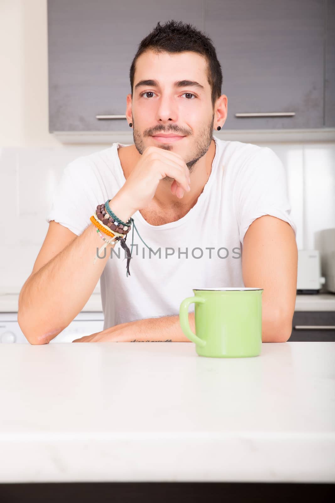 A young man sitting in the kitchen and drinking coffee.