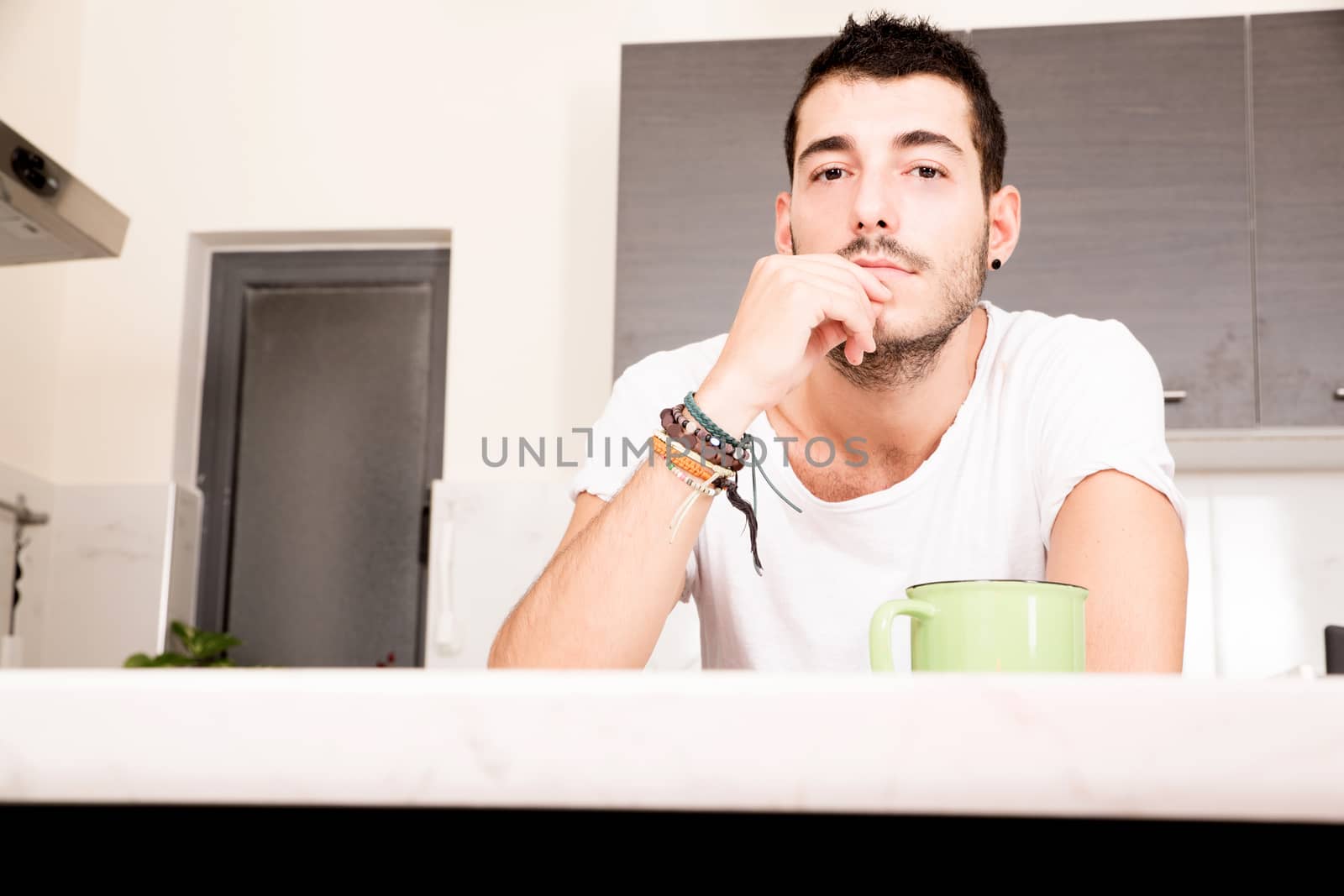 A young man sitting in the kitchen and drinking coffee.