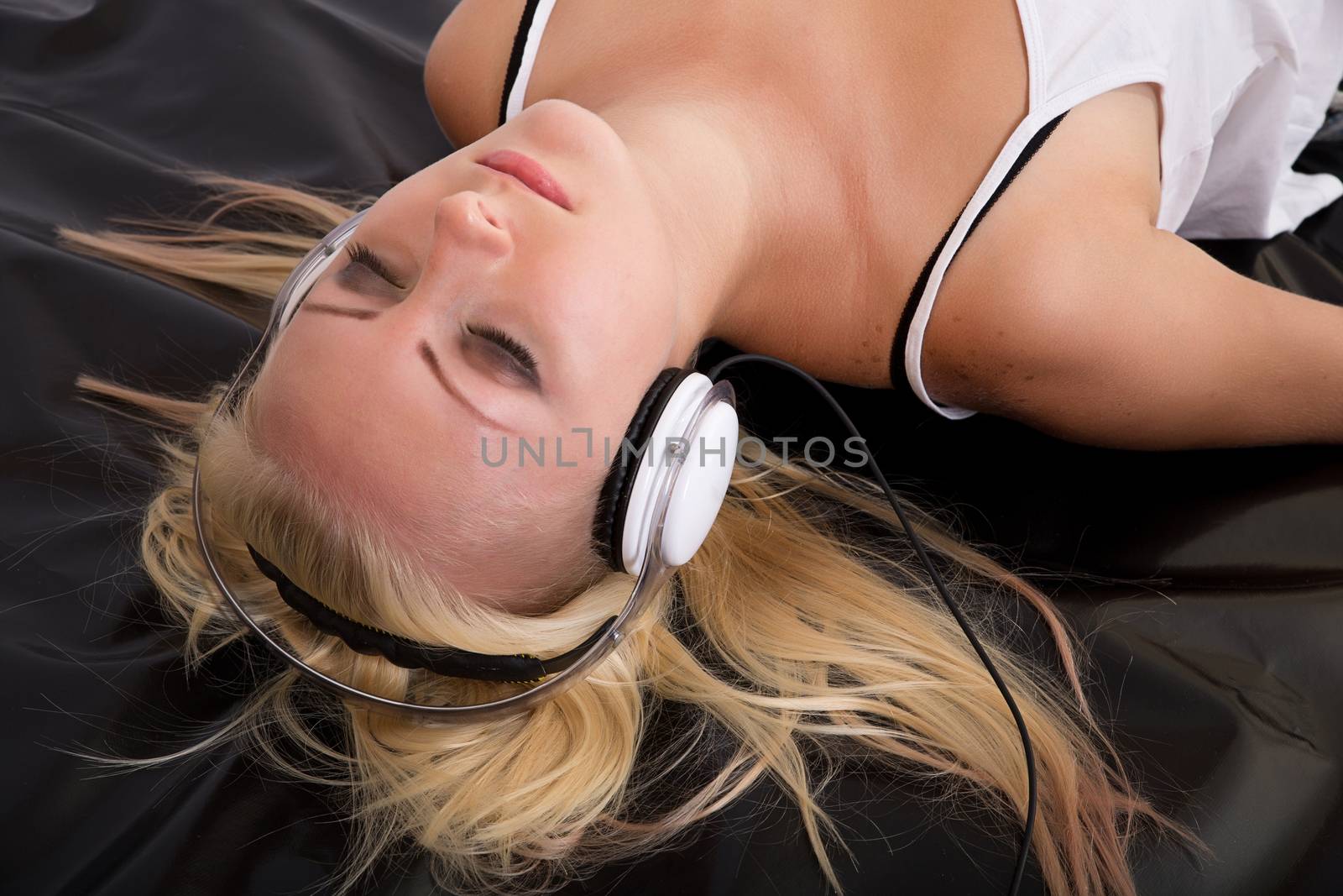 Portrait of a blonde girl lying on black latex with headphones.