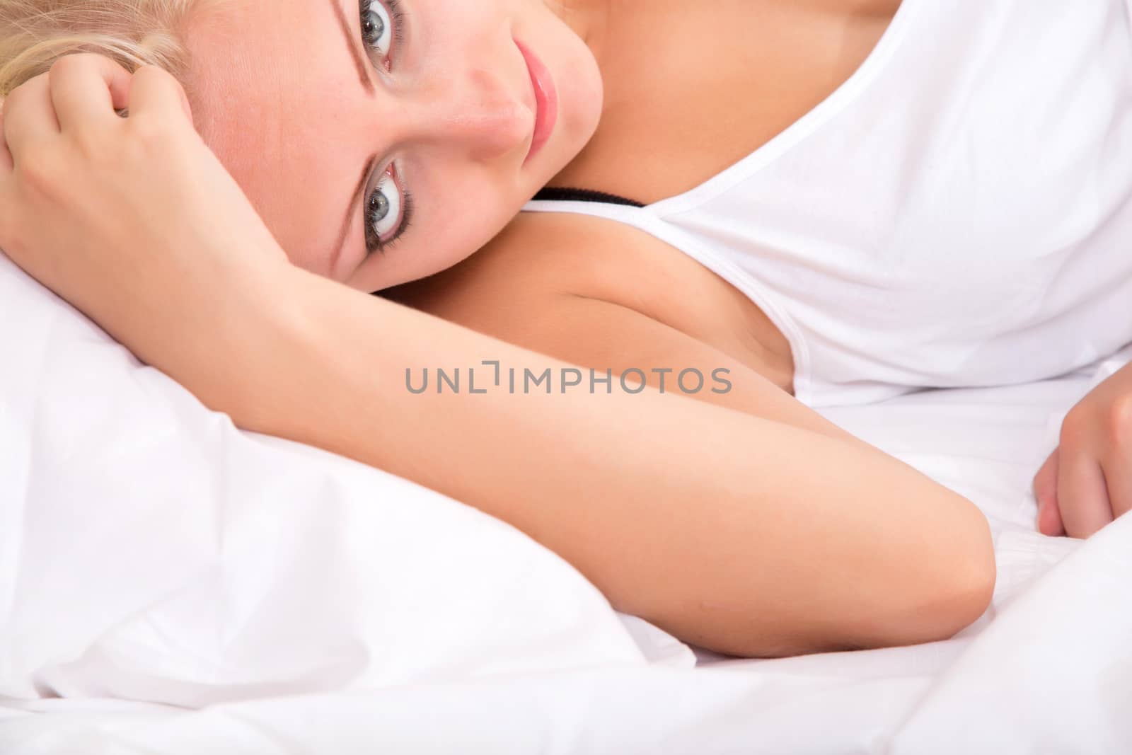 Portrait of a blonde girl lying sideways in a bed.