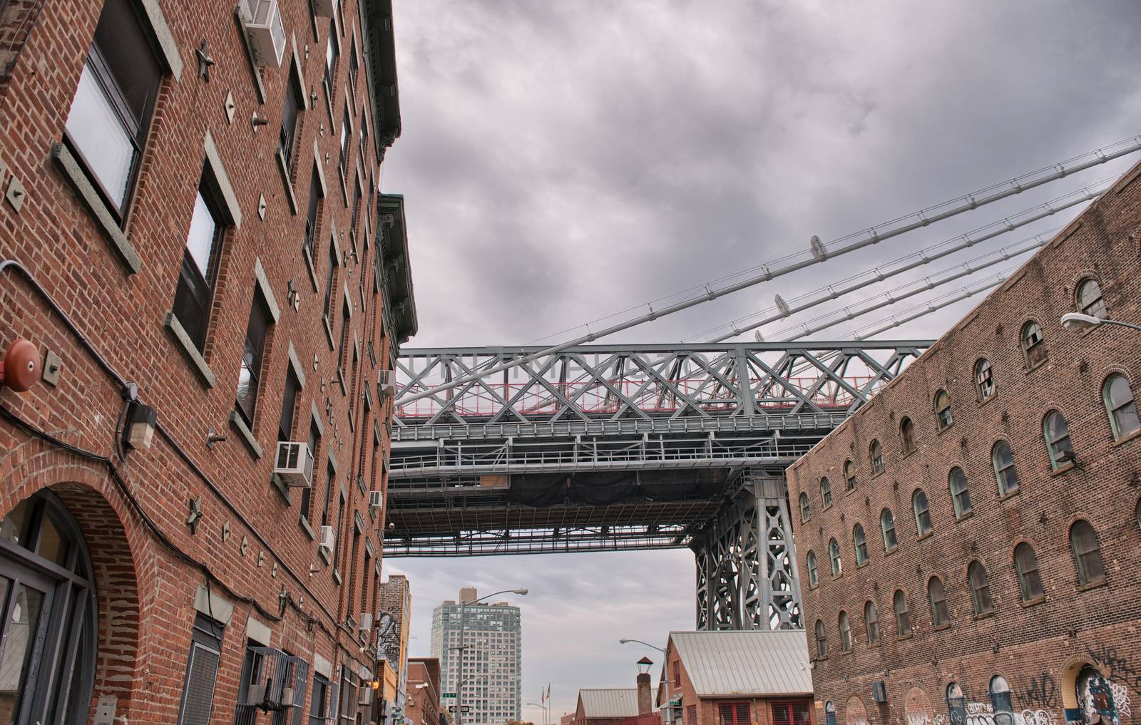 Metallic structure of Manhattan Bridge among classic Brooklyn buildings, New York City.