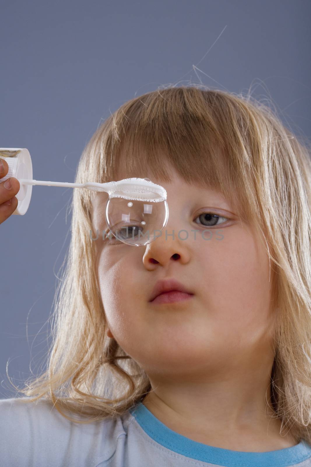 boy with long blond hair looking at big soap bubble - isolated on gray