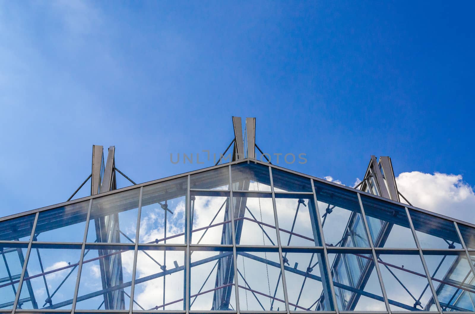 Glass roof in a steel structure against a blue sky with clouds.