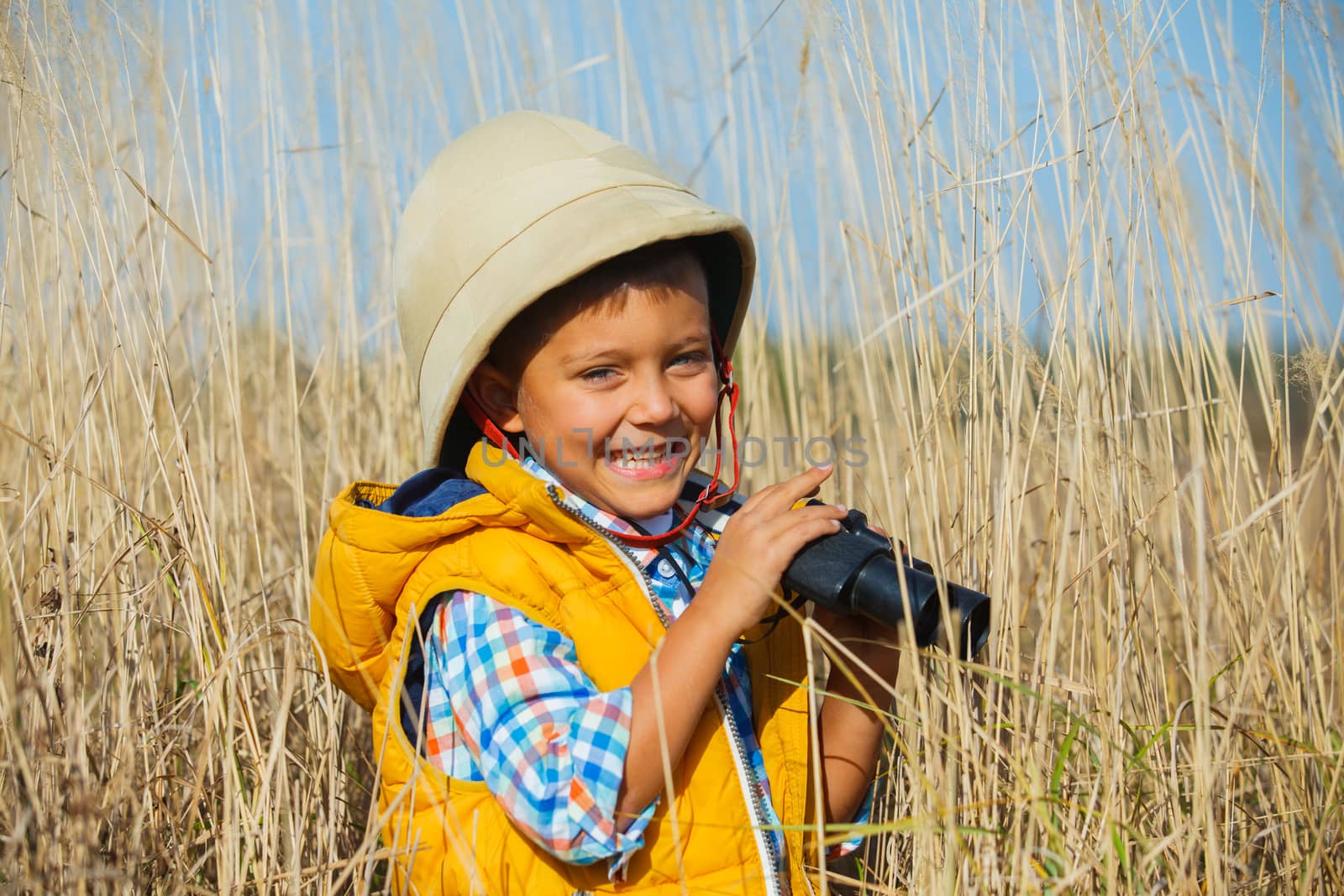 Young boy child playing pretend explorer adventure safari game outdoors with binoculars and bush hat