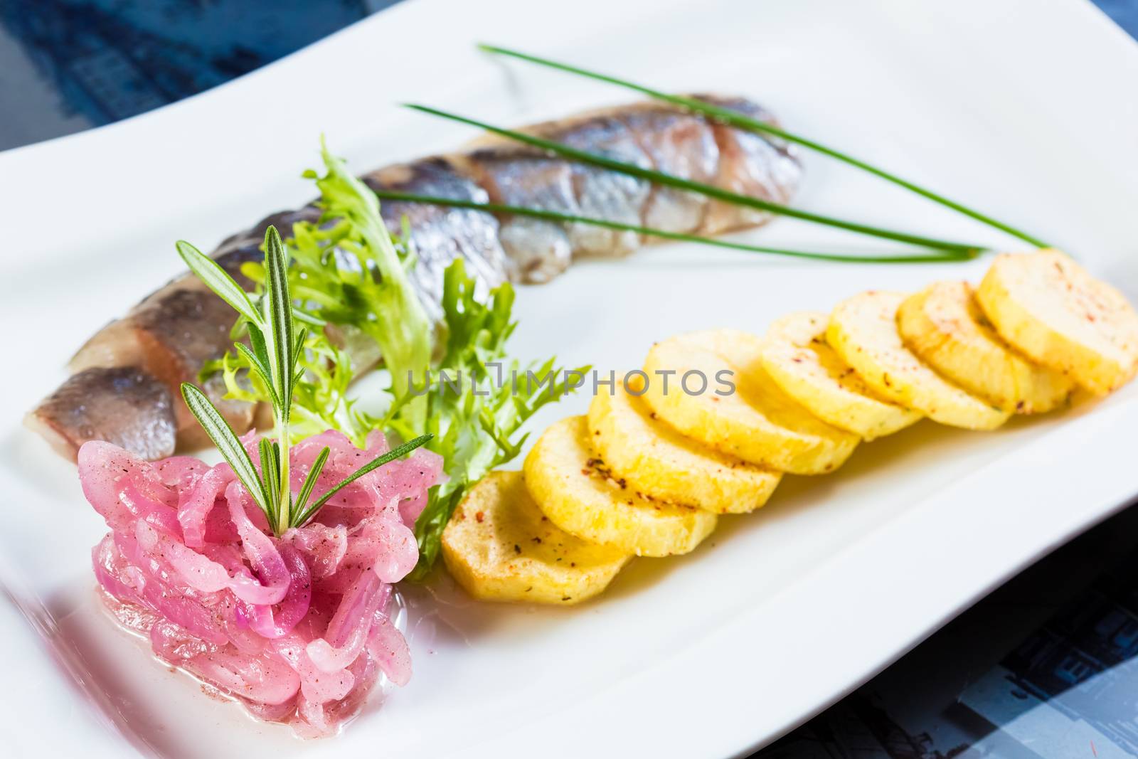 Herring with fried potatoes and red onions on a white plate