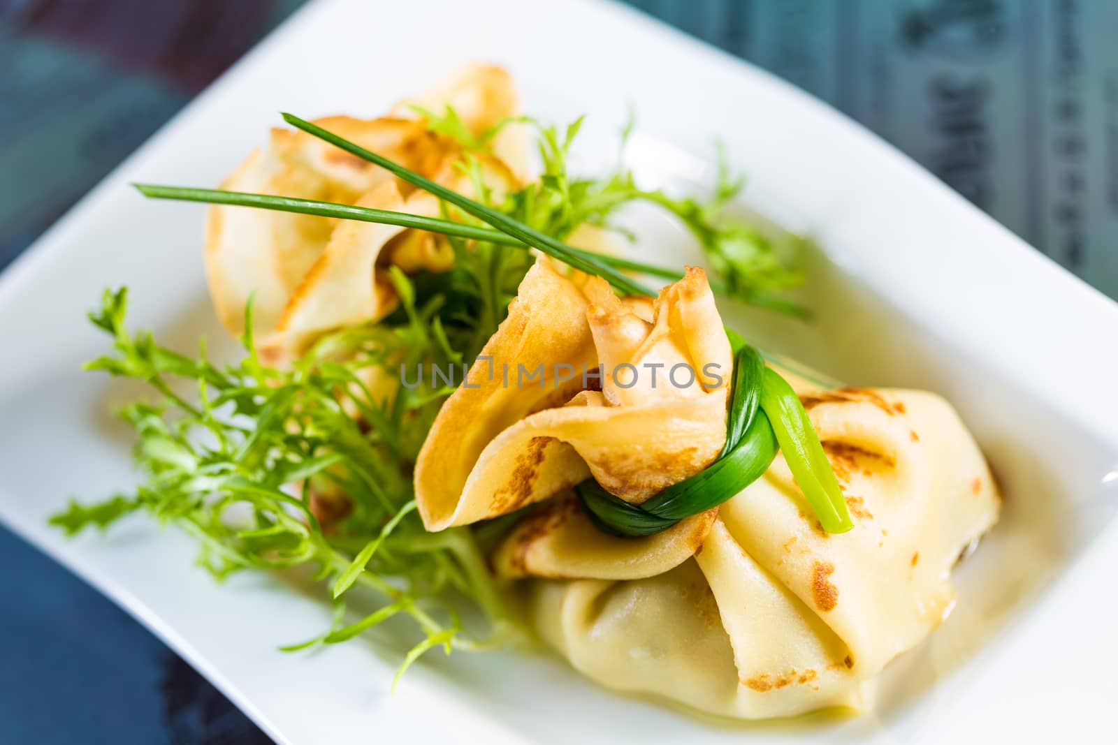 pancakes with meat decorated green onions on a white plate