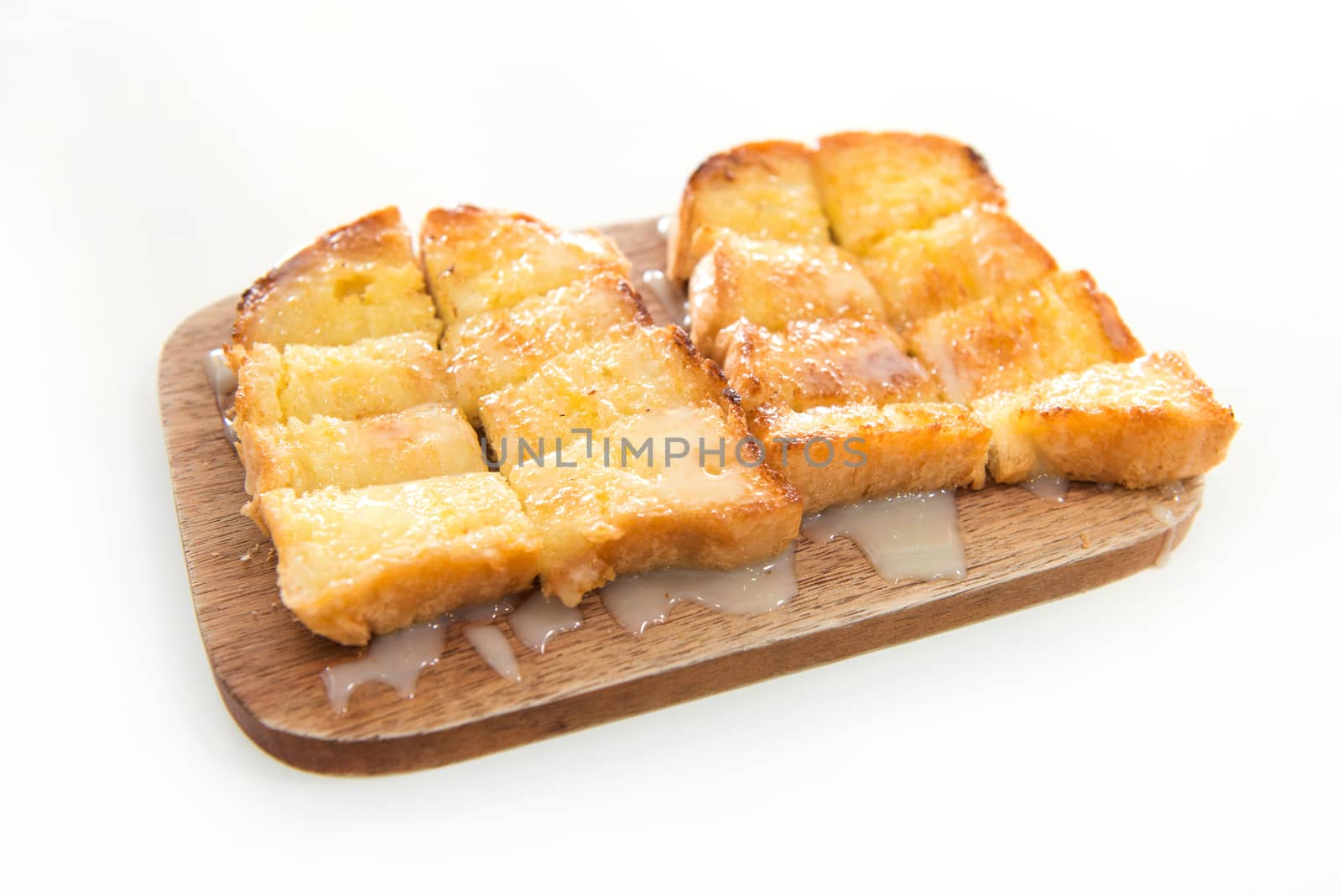 Bread toast and condensed milk on wooden plate over white background