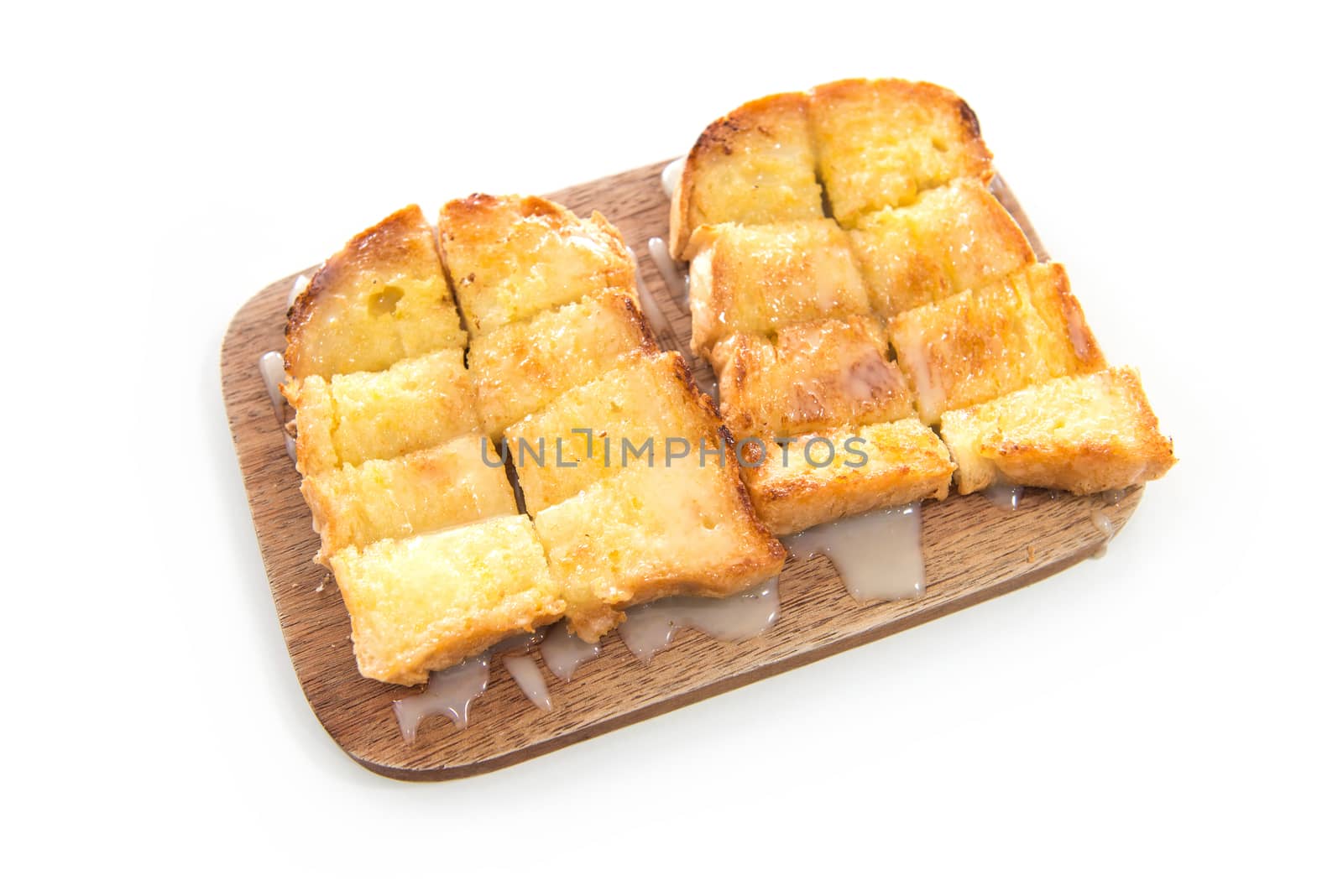 Bread toast and condensed milk on wooden plate over white background