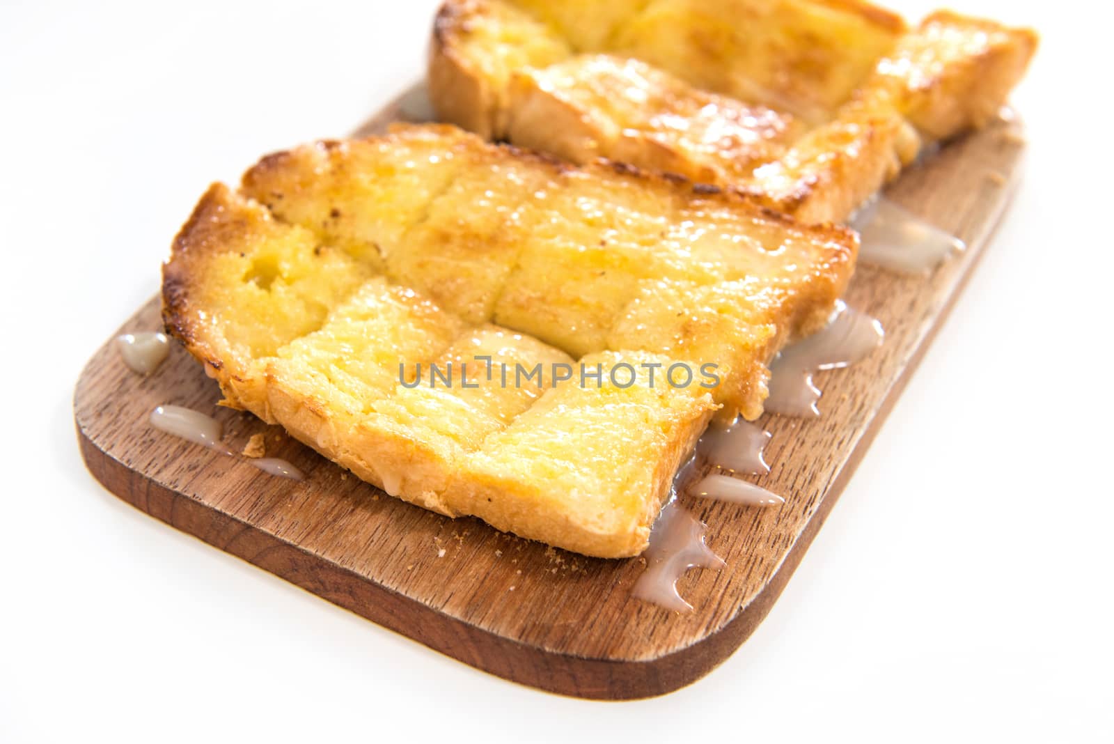 Bread toast and condensed milk on wooden plate over white background