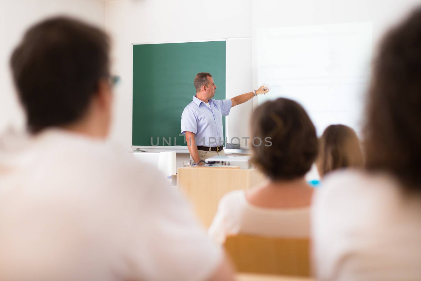 Teacher at university in front of a whiteboard screen. Students listening to lecture and making notes.