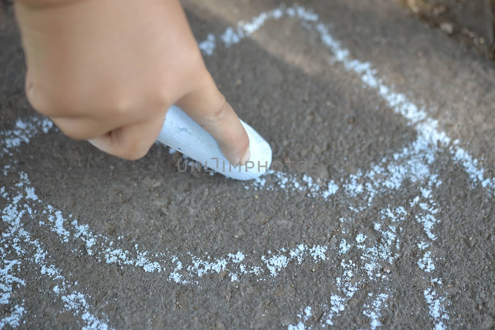 Child hand drawing with chalk on the ground