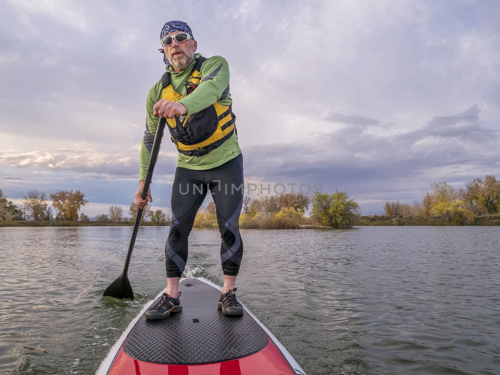 senior paddler in life jacket enjoying stand up paddling on lake, fall scenery in Fort Collins, Colorado