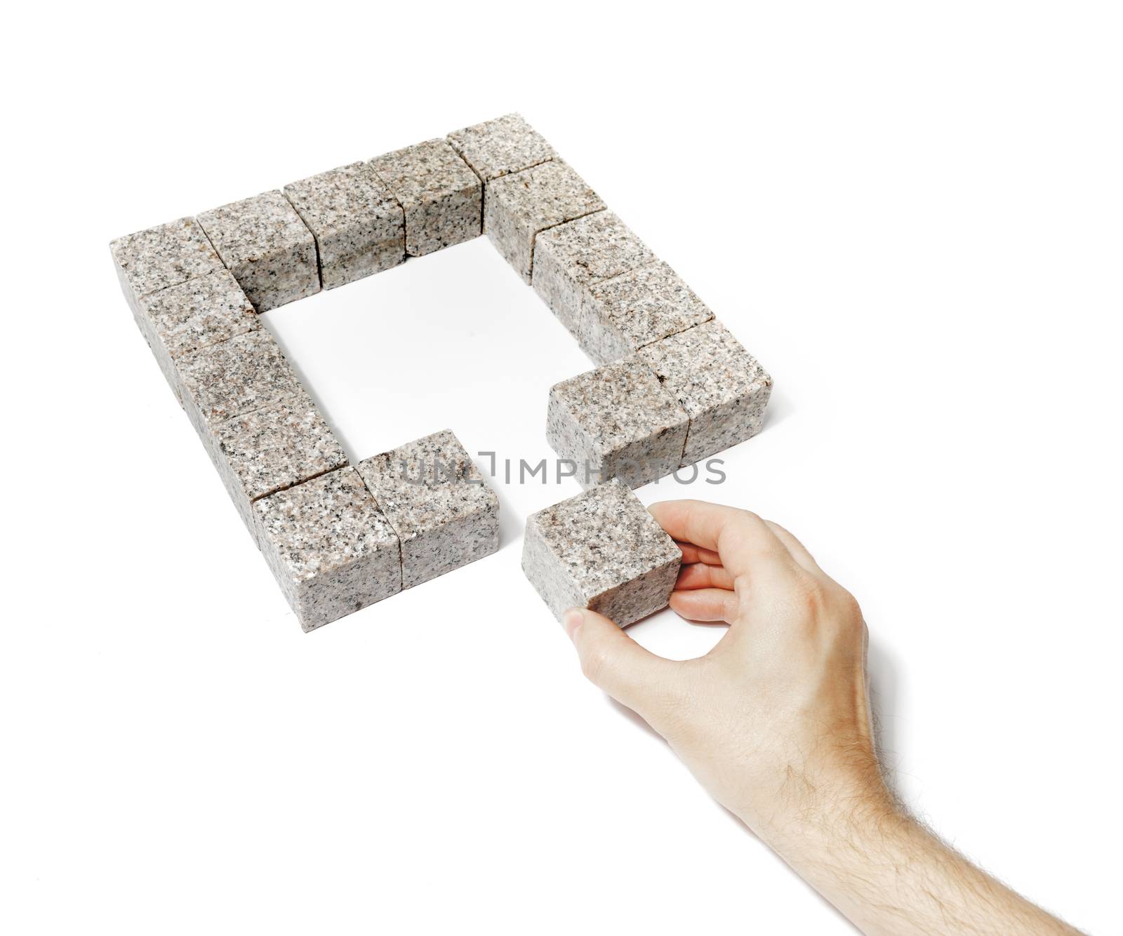 Man finishing a square made of small blocks of granite rock.