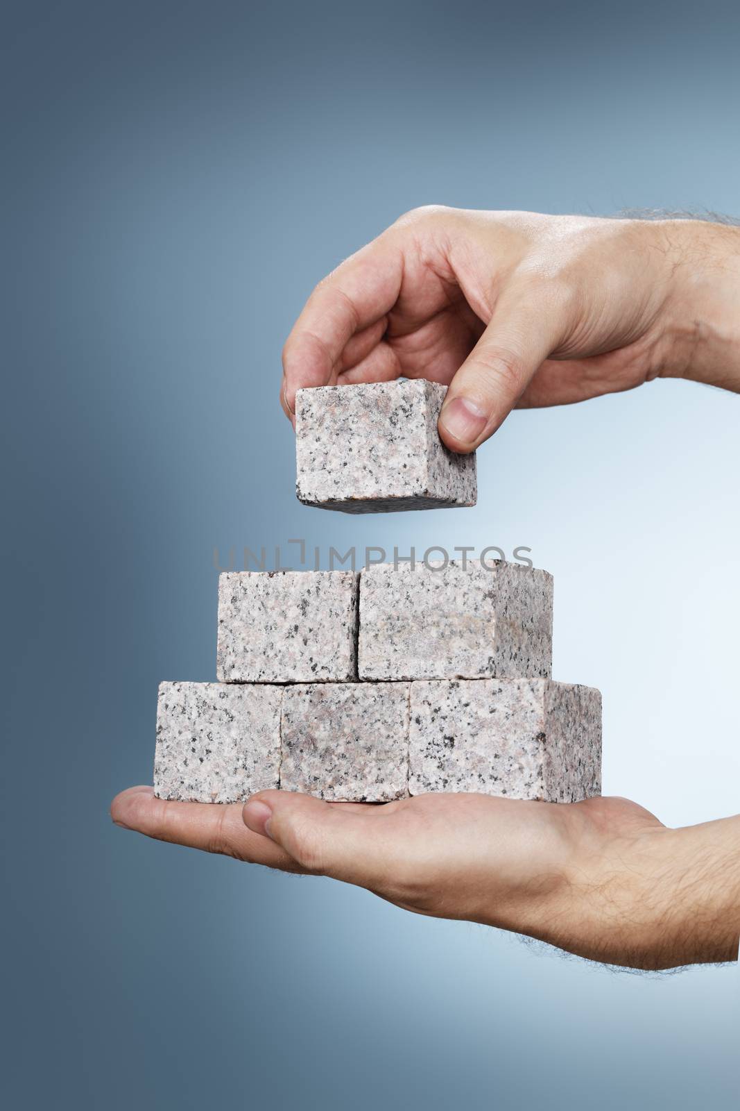 Man building a pyramid of granite rock blocks in his hands.