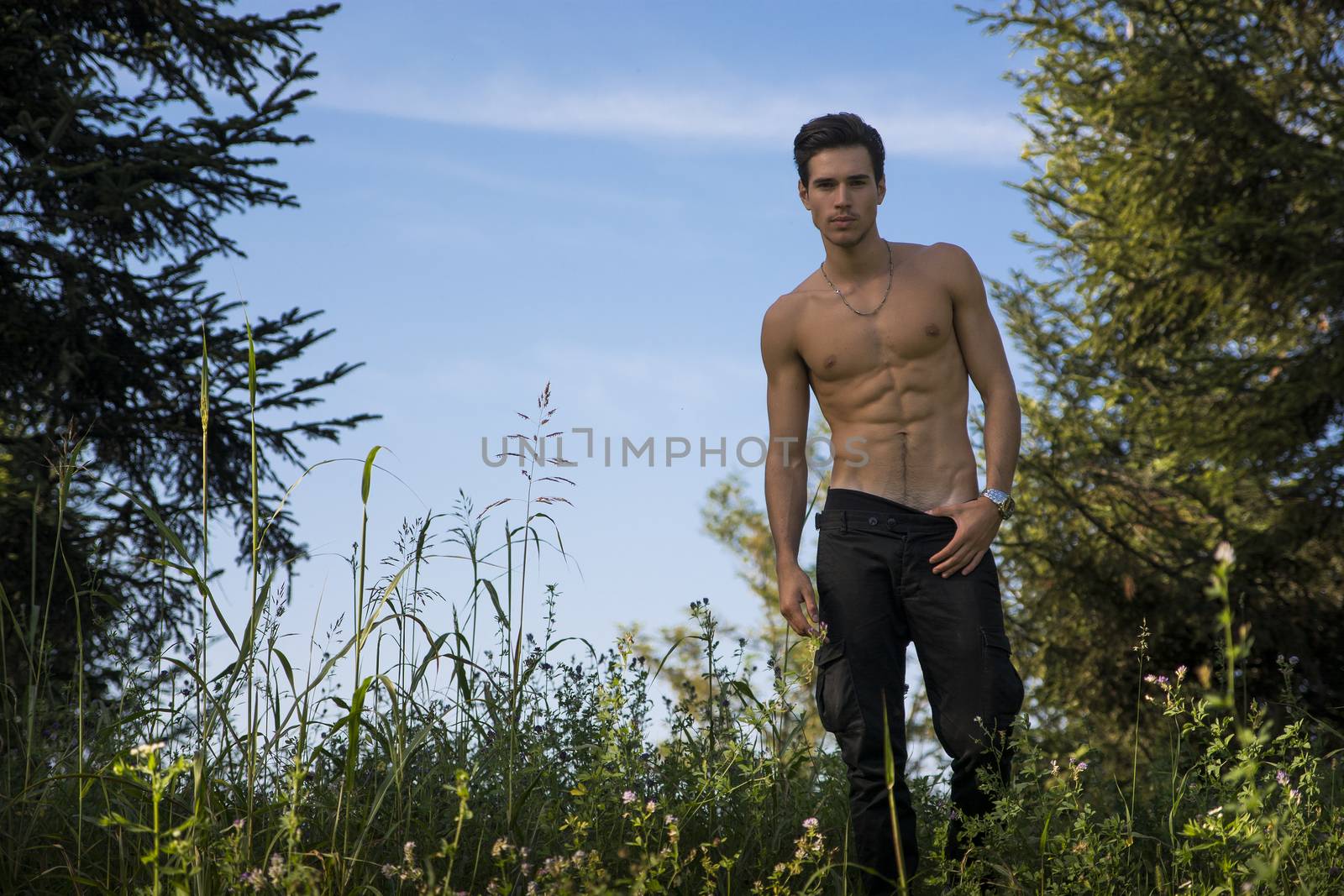 Gorgeous Young Shirtless Man with Sexy Abs, Strike a Pose at the Garden While Looking at the Camera.
