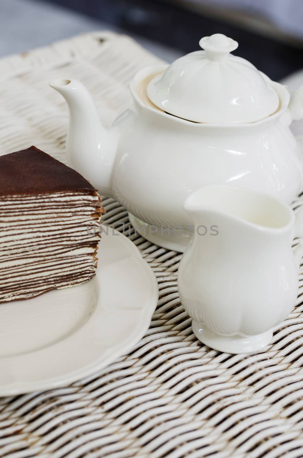 Teapot with chocolate crape cake on weave texture table