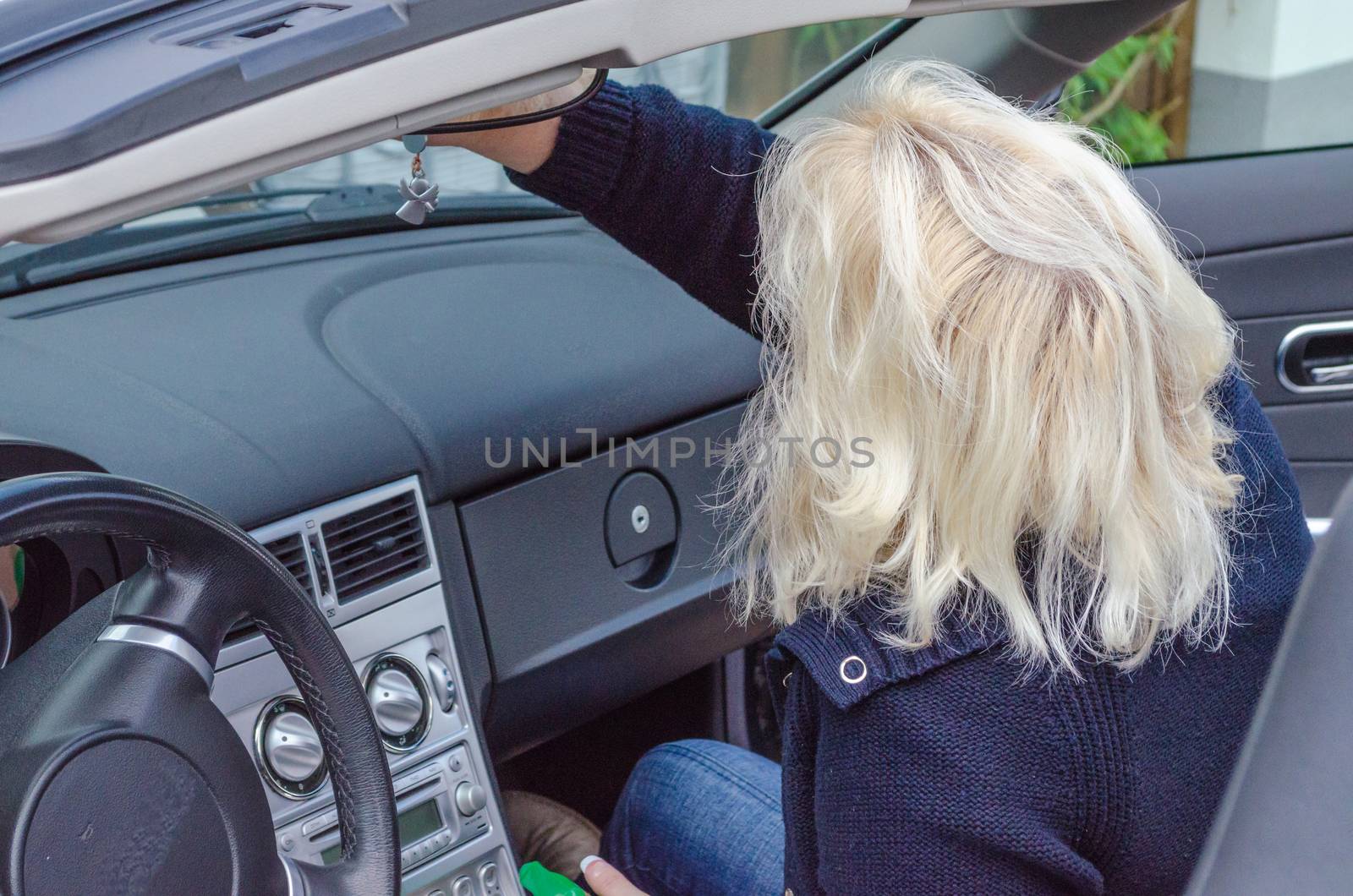 Woman with blond hair cleans the windshield of a convertible.
