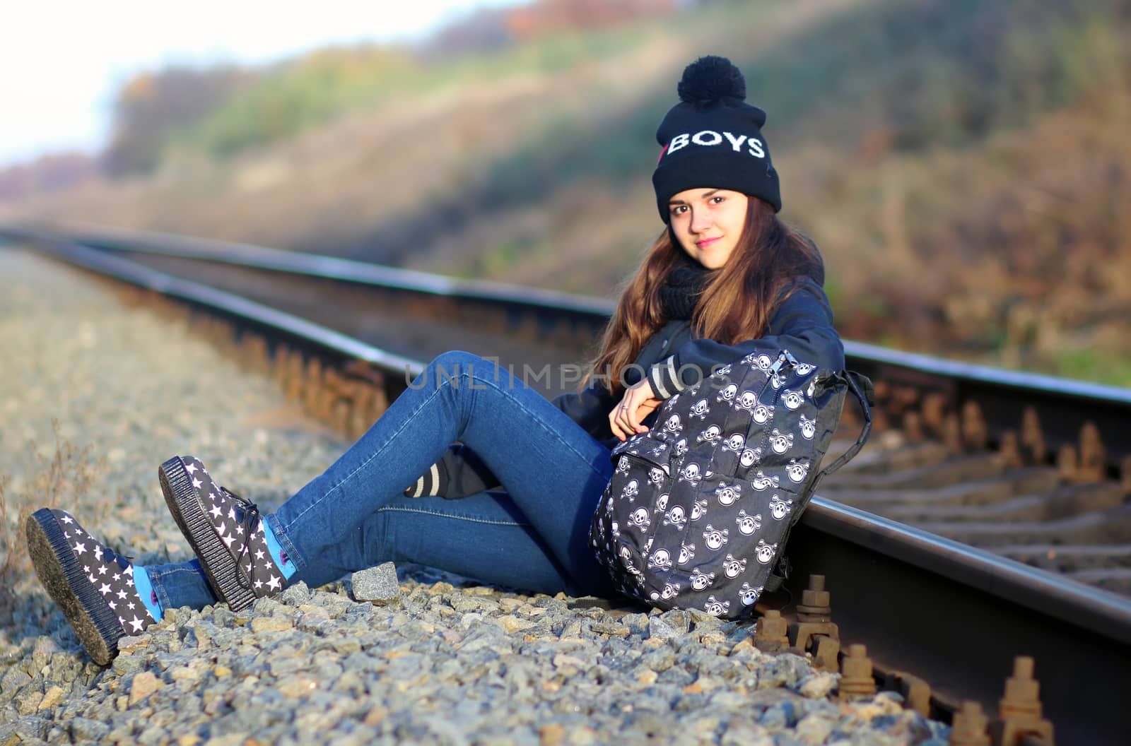 A girl sitting near the railway at sunset