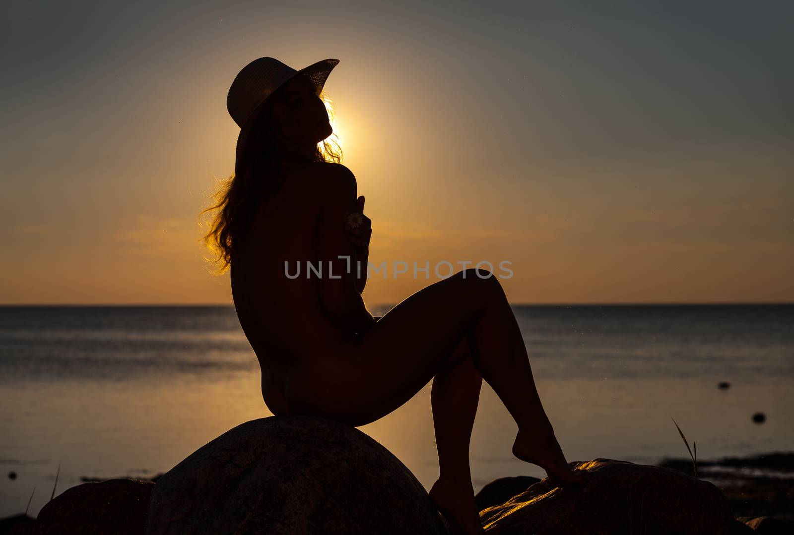 Silhouette of a young naked woman posing on the beach in the evening sun