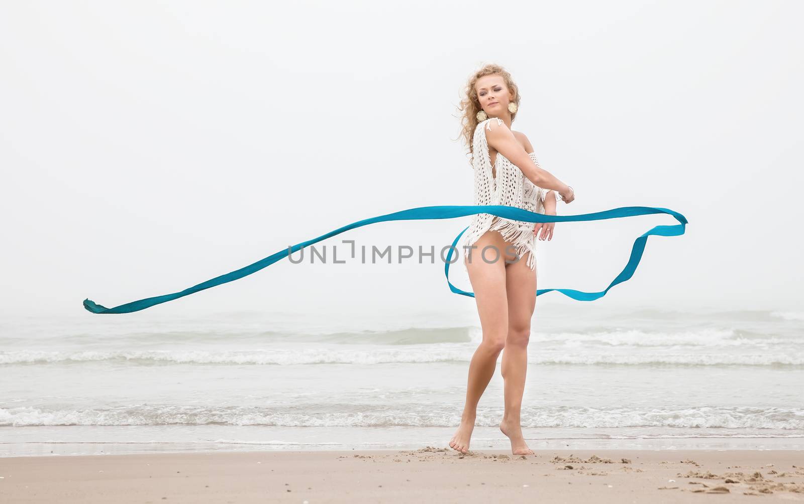 Young beautiful gymnast woman dance with ribbon on the beach at foggy day