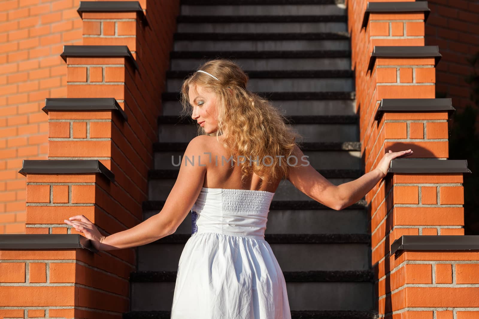 Coquettish young beautiful woman posing near the stairs at sunset