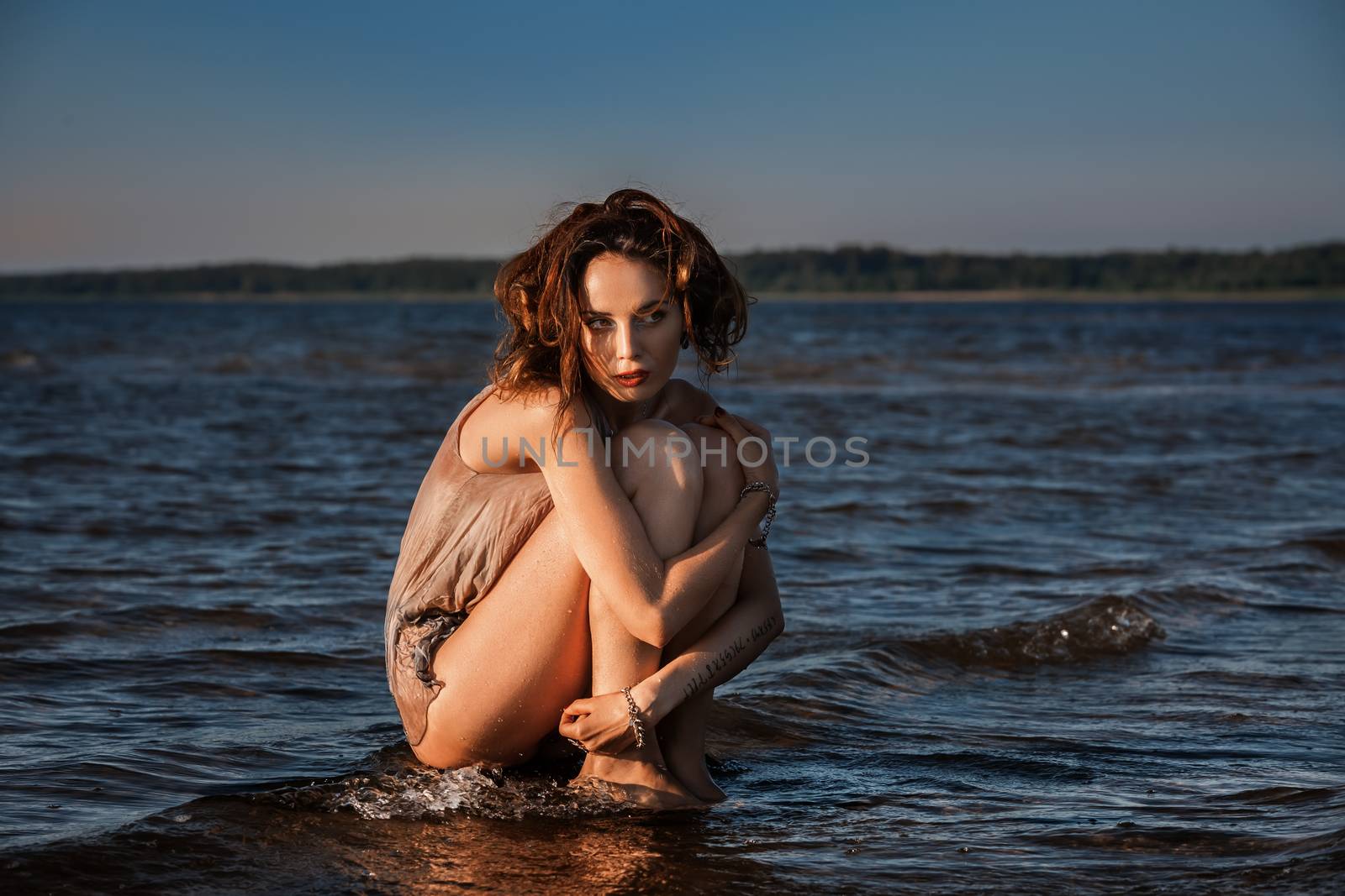 Attractive young seminude woman in a wet suit posing against the sea background. Evening light with deep shadows and color shift