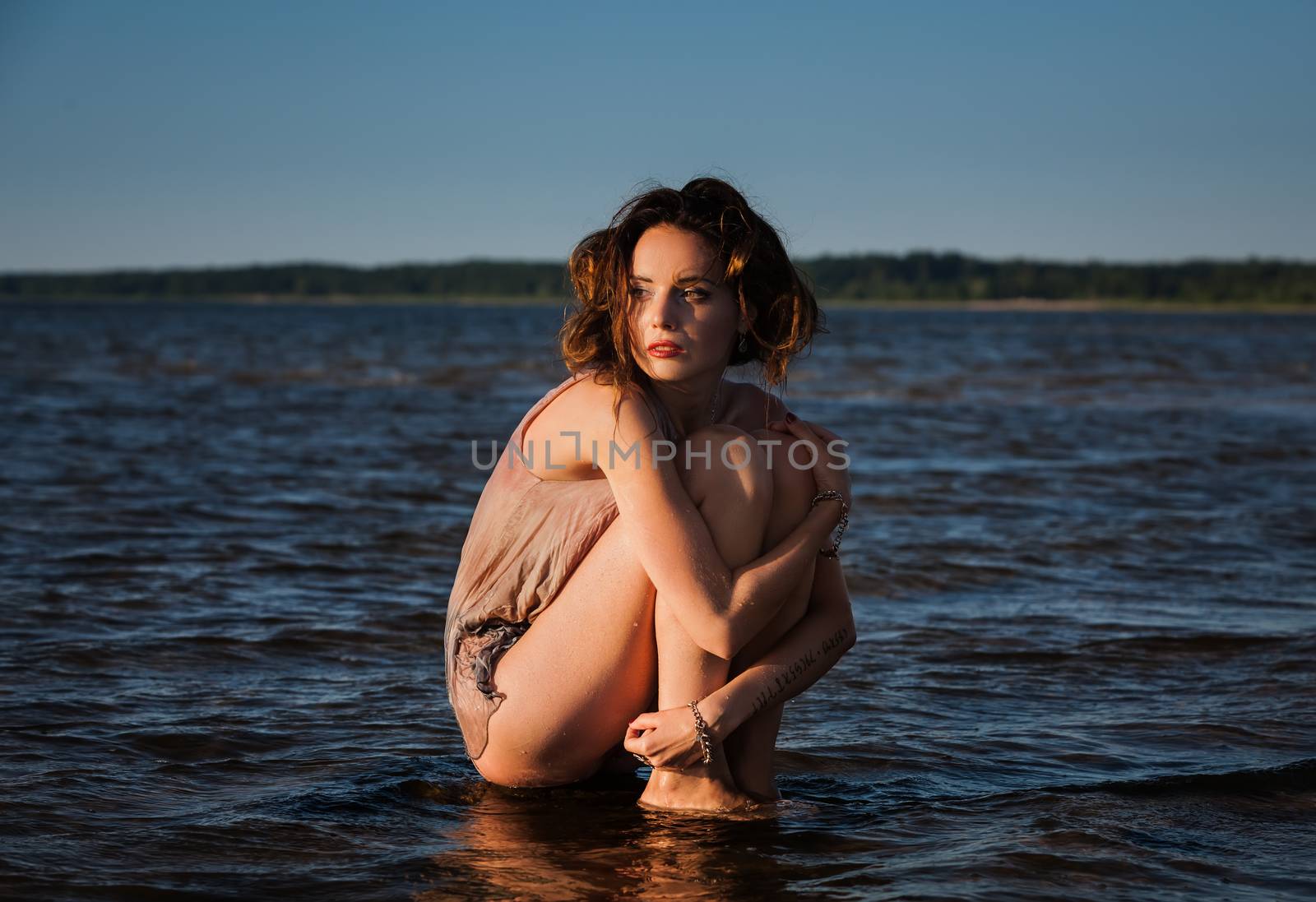 Attractive young seminude woman in a wet suit posing against the sea background