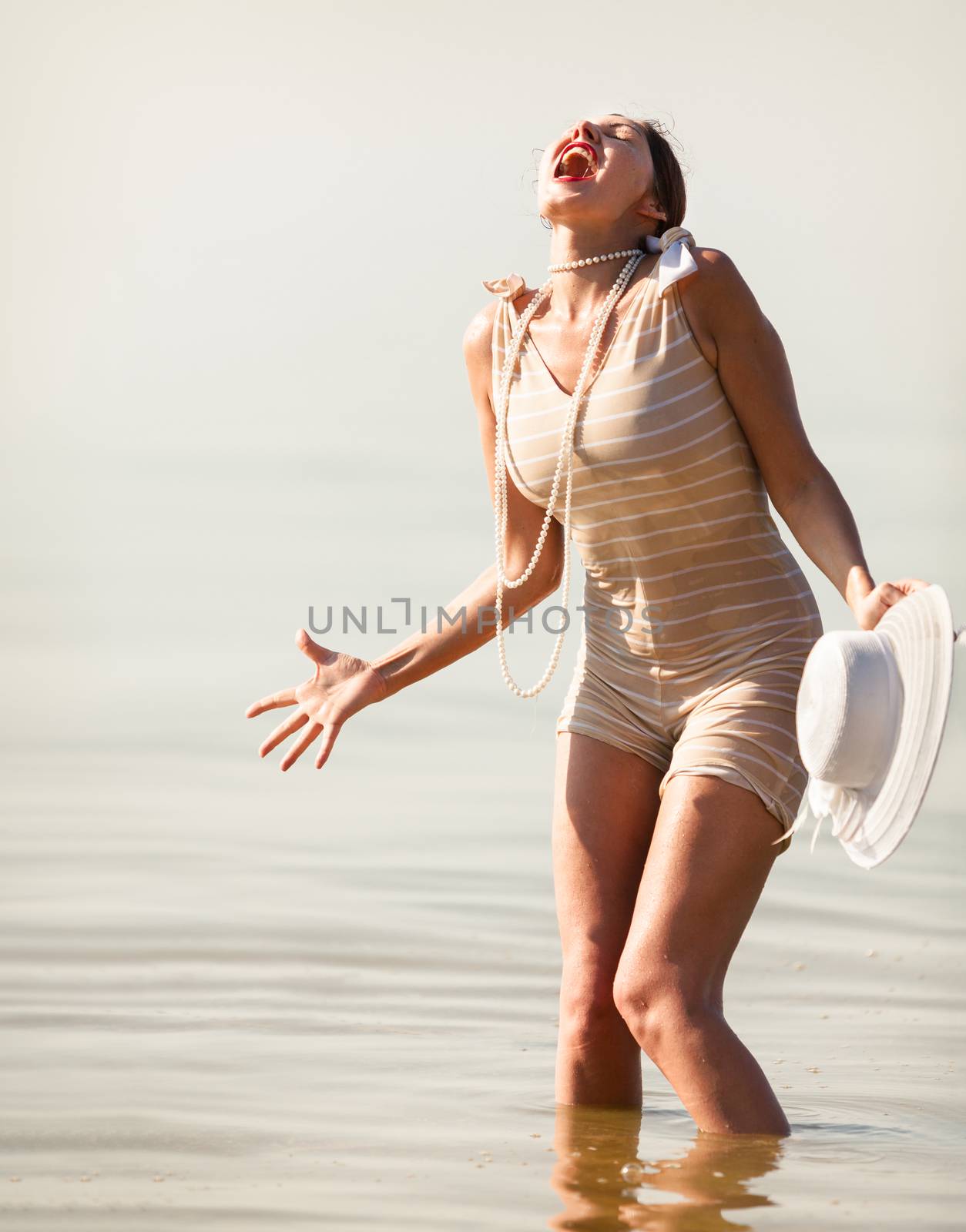 Woman in a striped retro bathing suit in the white hat screams against the sea