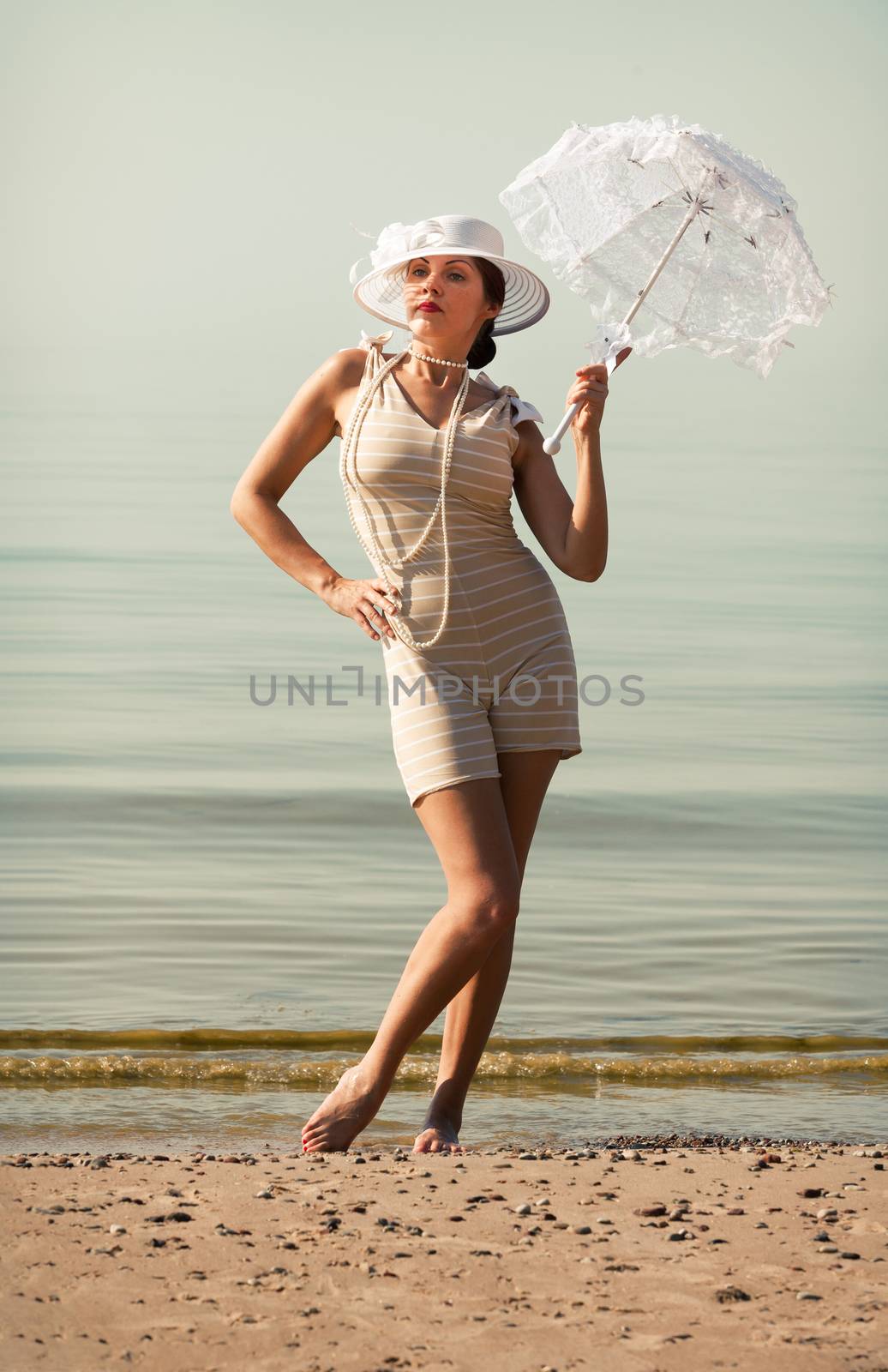 Woman in a striped retro bathing suit with a white parasol against the sea