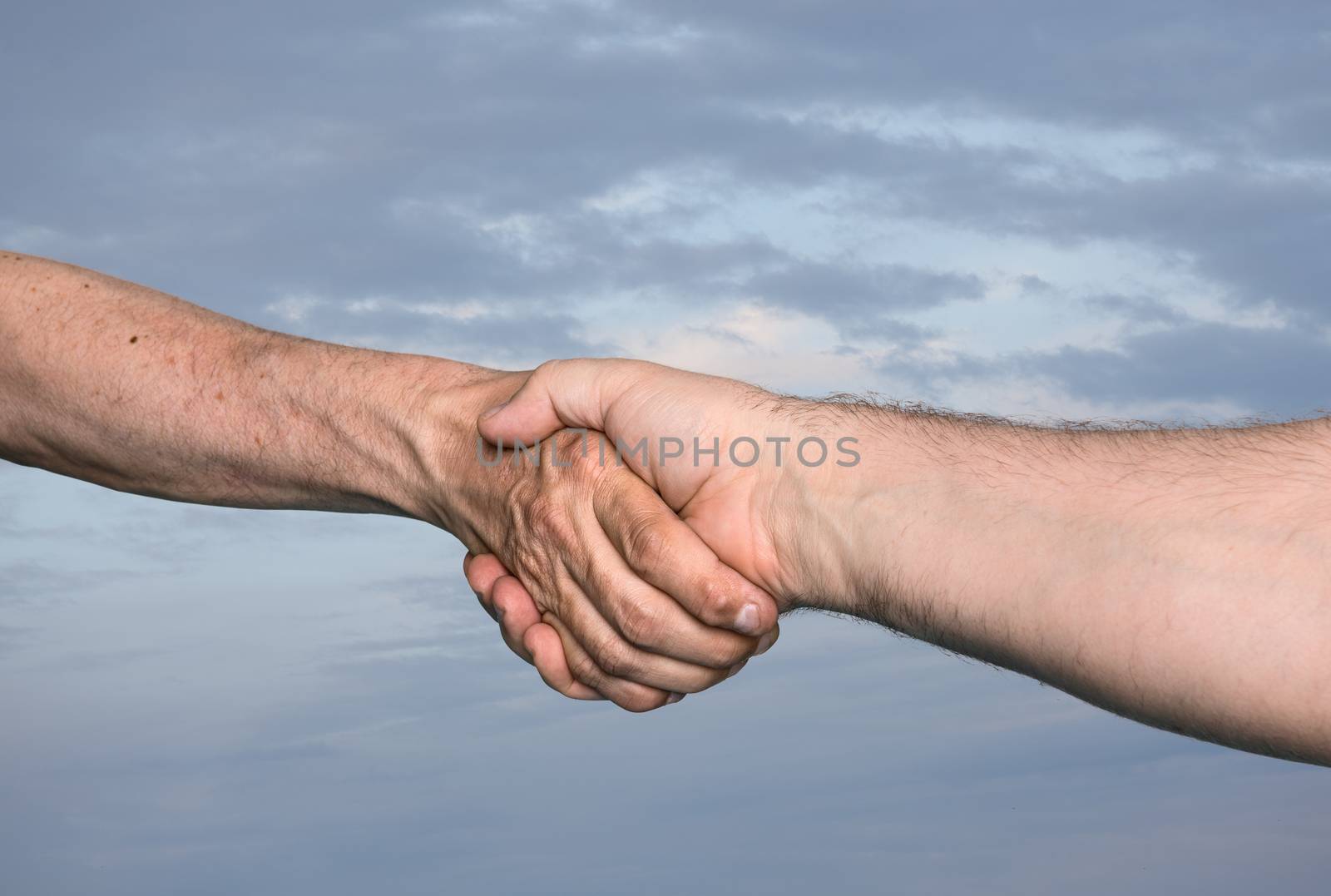Handshaking. Shaking hands of two male people against of the cloudy sky