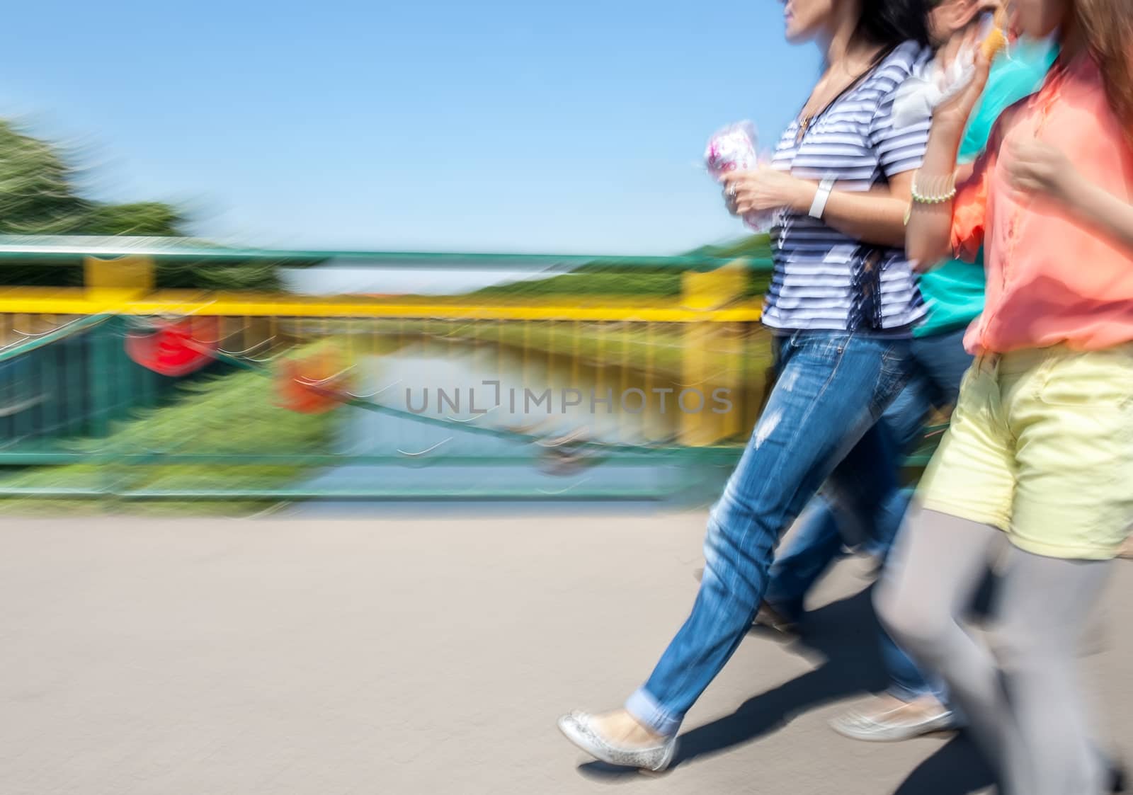 Group of girls walking on the bridge with ice cream in their hands. Intentional motion blur