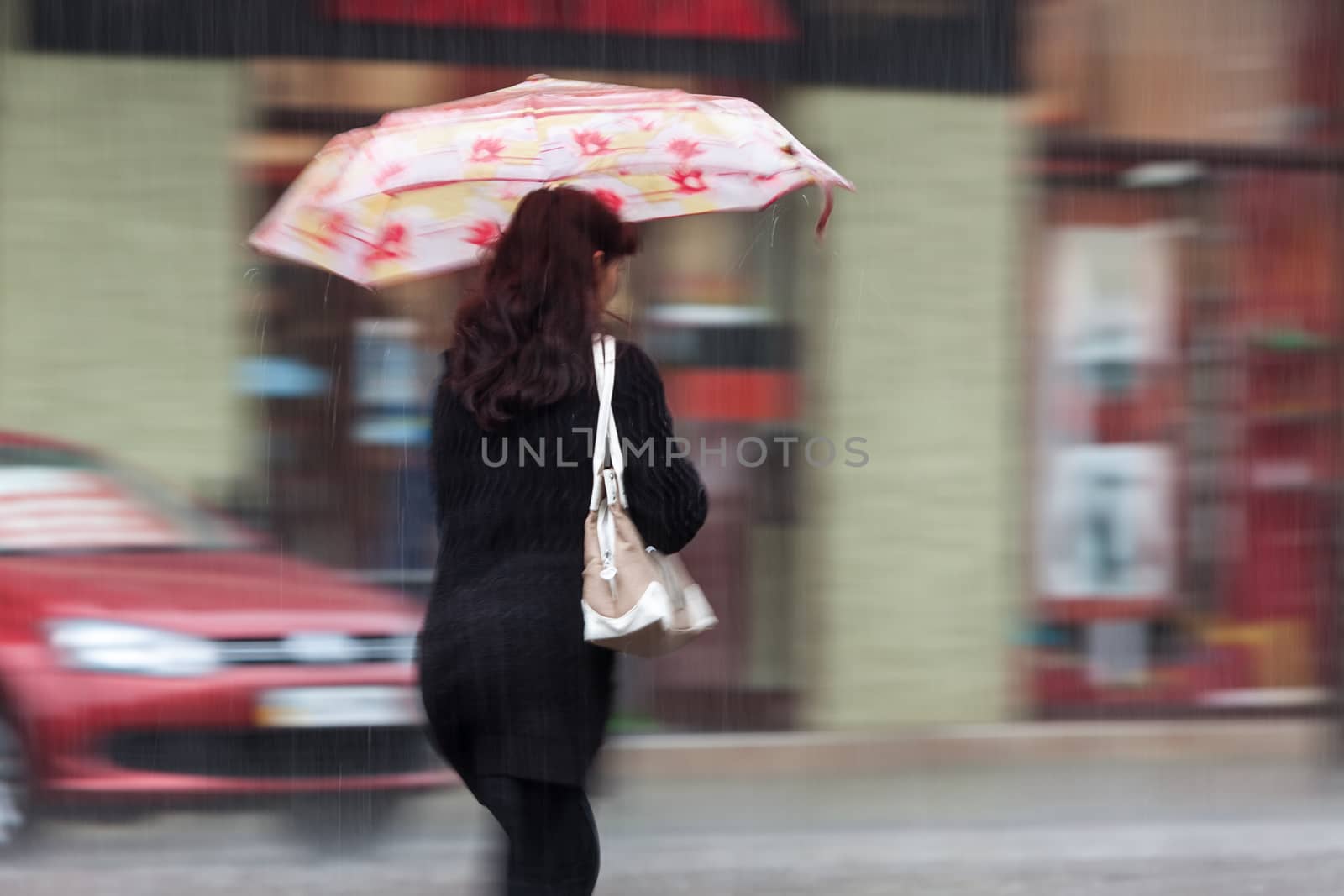 Shower. Woman walking down the street in rainy day. Intentional motion blur