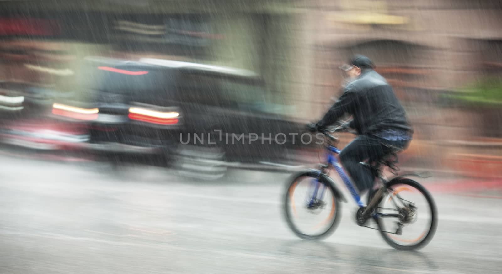Rainfall in the city. Wet cyclist rides through the streets on a rainy day. Intentional motion blur
