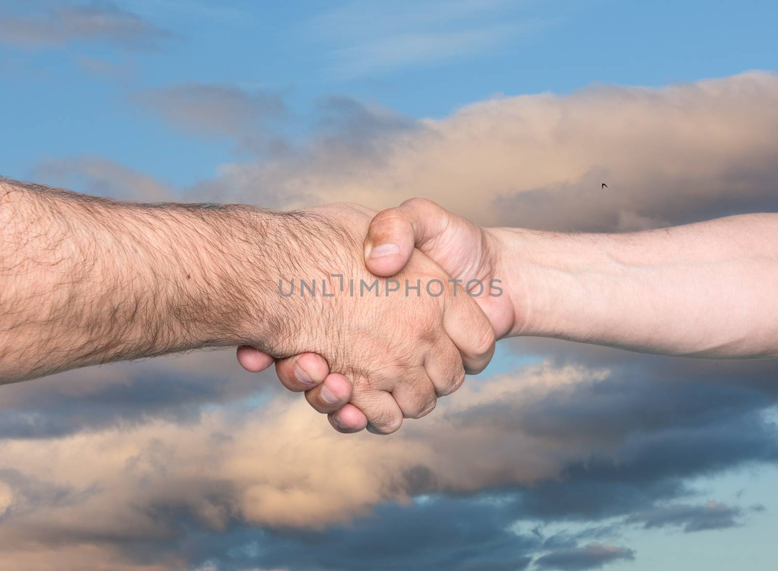 Handshaking. Shaking hands of two male people on cloudy sky background
