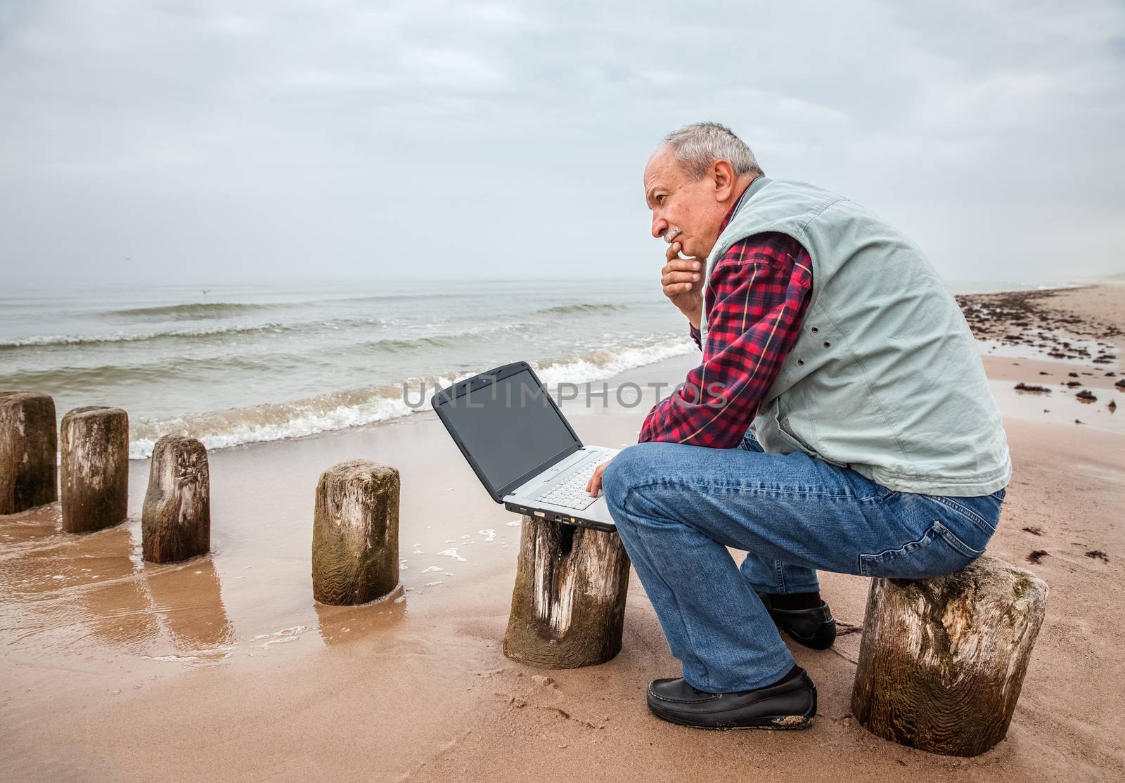 Thoughtful elderly man with the laptop sits on a sea background