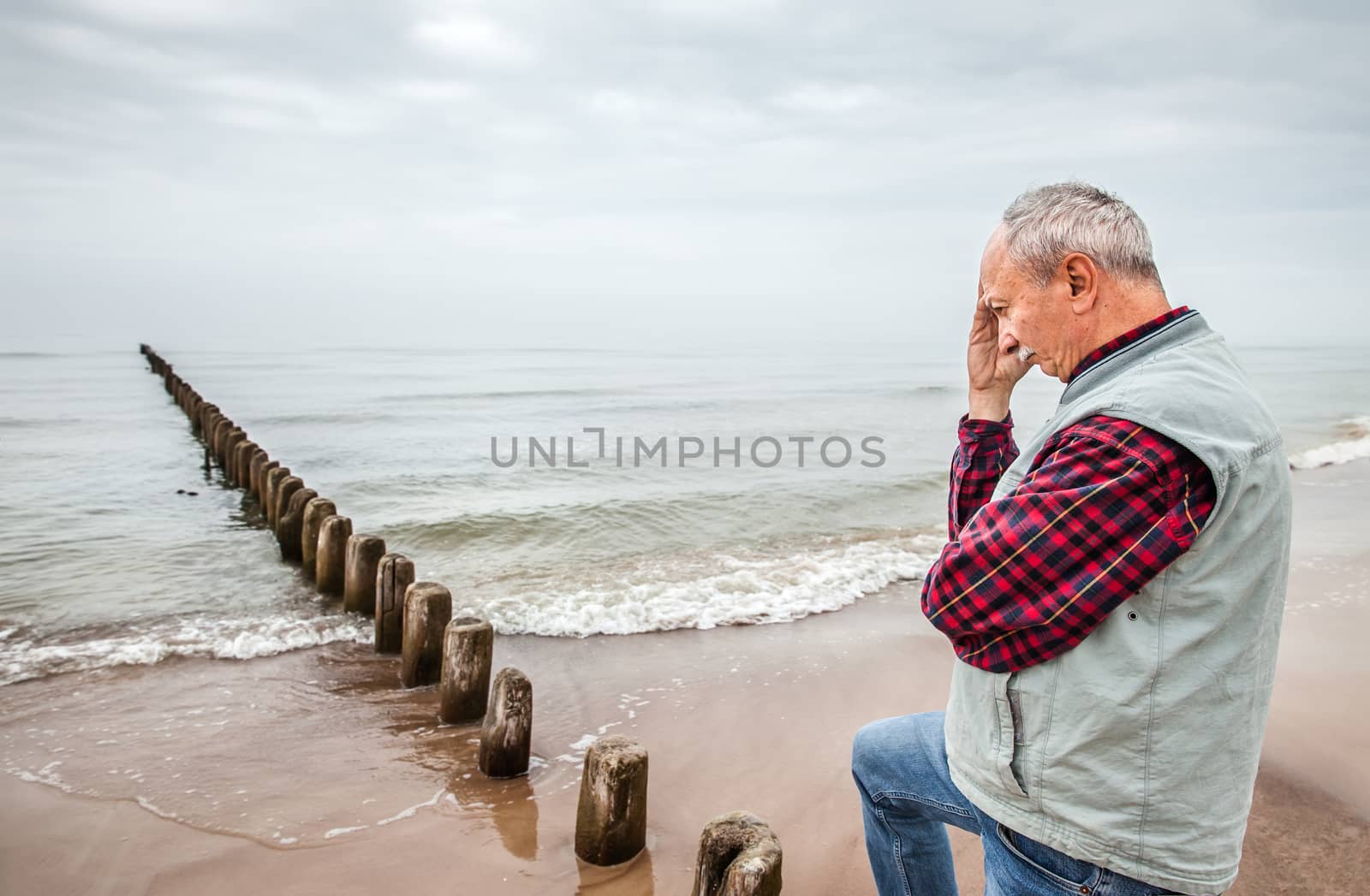 Thoughtful elderly man standing on the beach on a foggy day