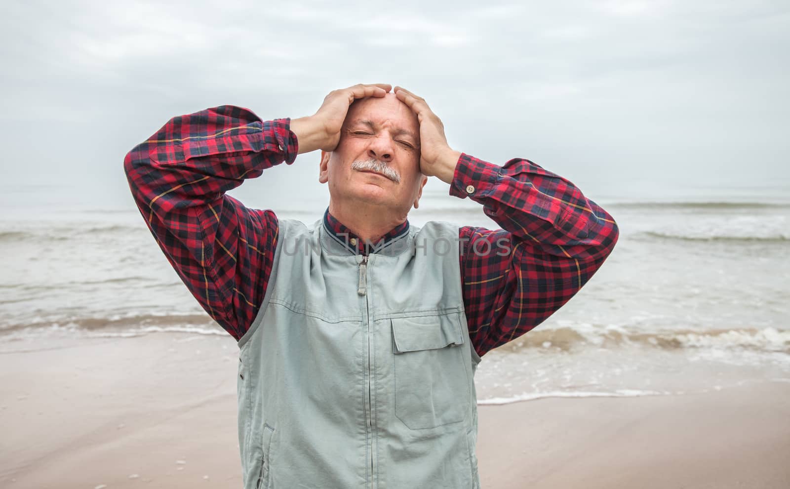 Elderly man suffering from a headache on sea background on foggy day