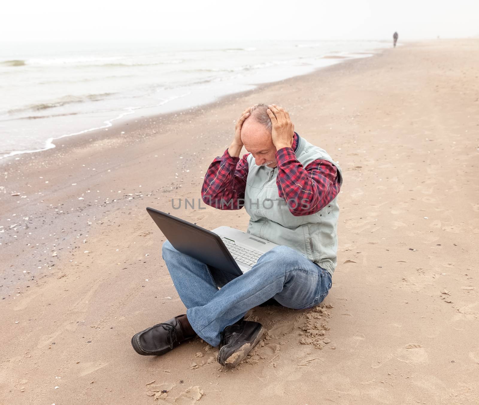 Problems. Senior businessman sitting with notebook on beach